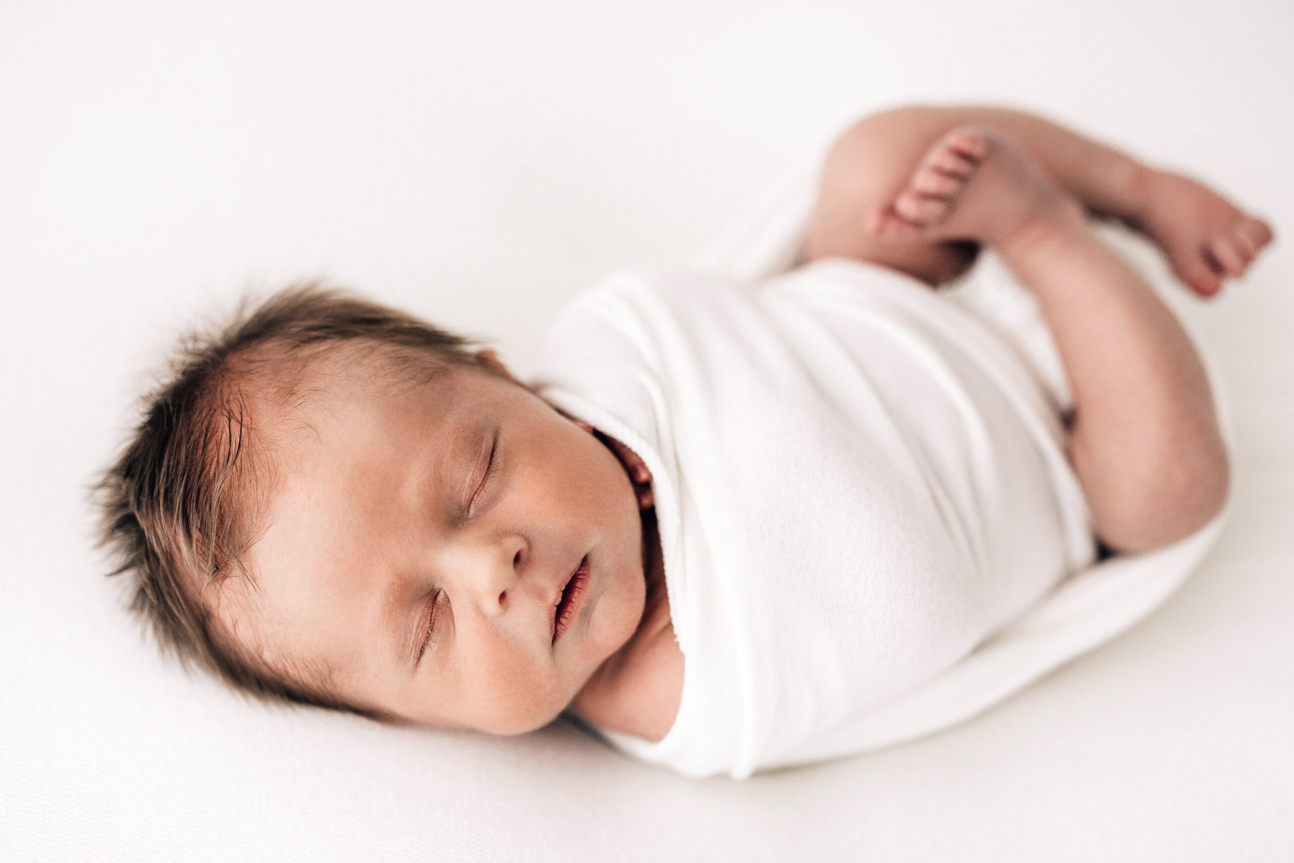 Newborn Sleeping on a white cloth and swaddled for newborn photos