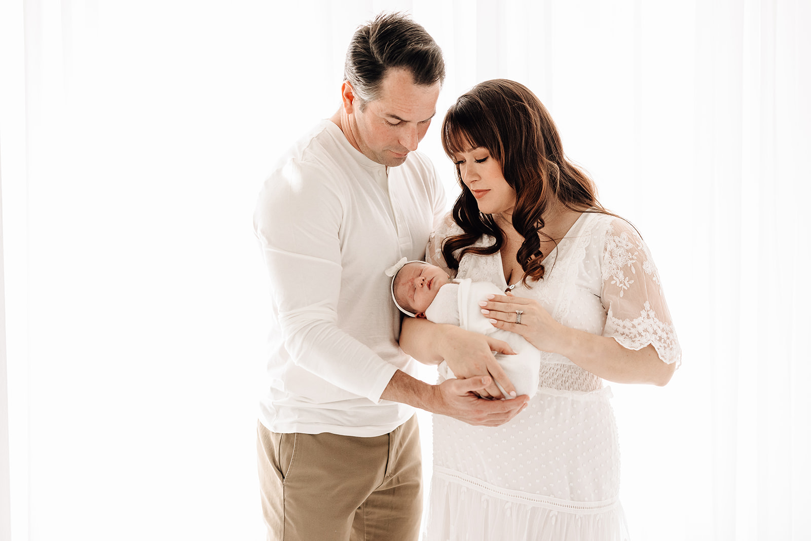 Happy new parents hold their newborn baby daughter while standing in a studio window
