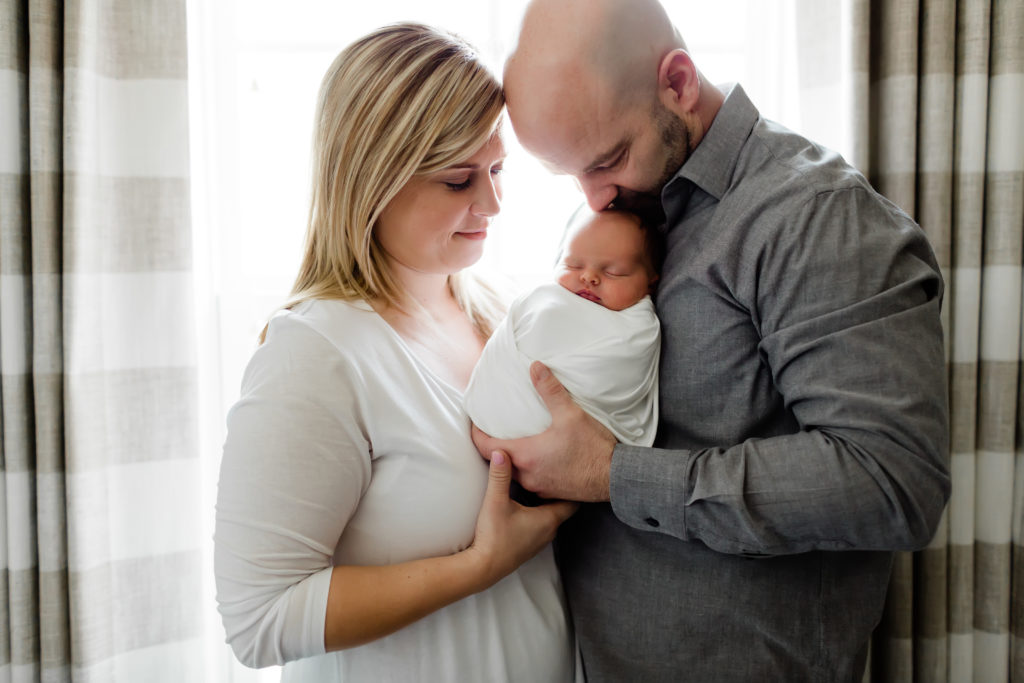 Mom and dad holding newborn in baby nursery window during a lifestyle photo session