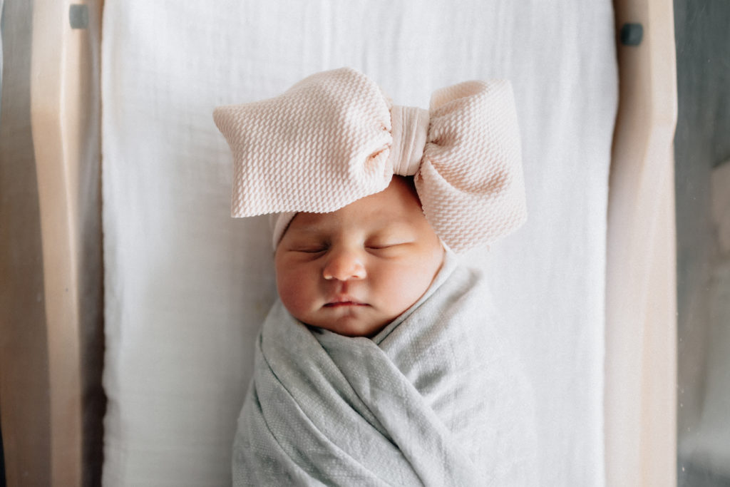 Newborn baby girl in hospital bassinet with large pink bow posing for a fresh 48 session