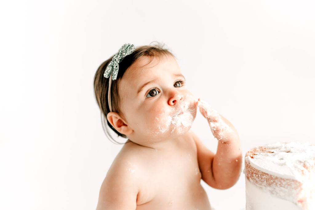 Brown eyed baby at 12 month cake smash session eating cake and white icing. 