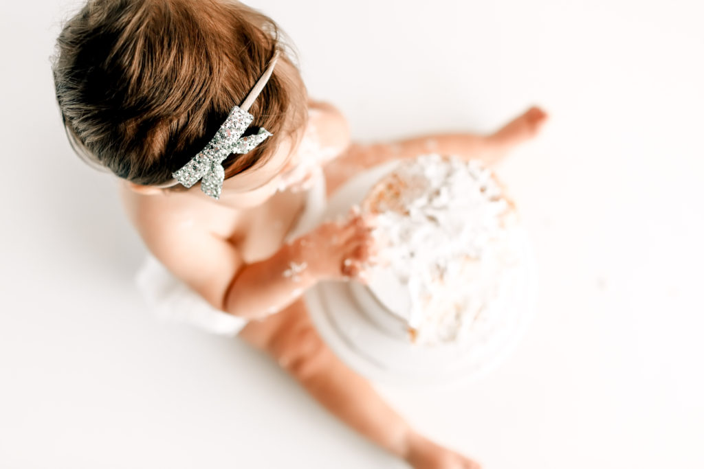 Baby wearing all white and glitter headband for cake smash session in st. Louis natural light studio 