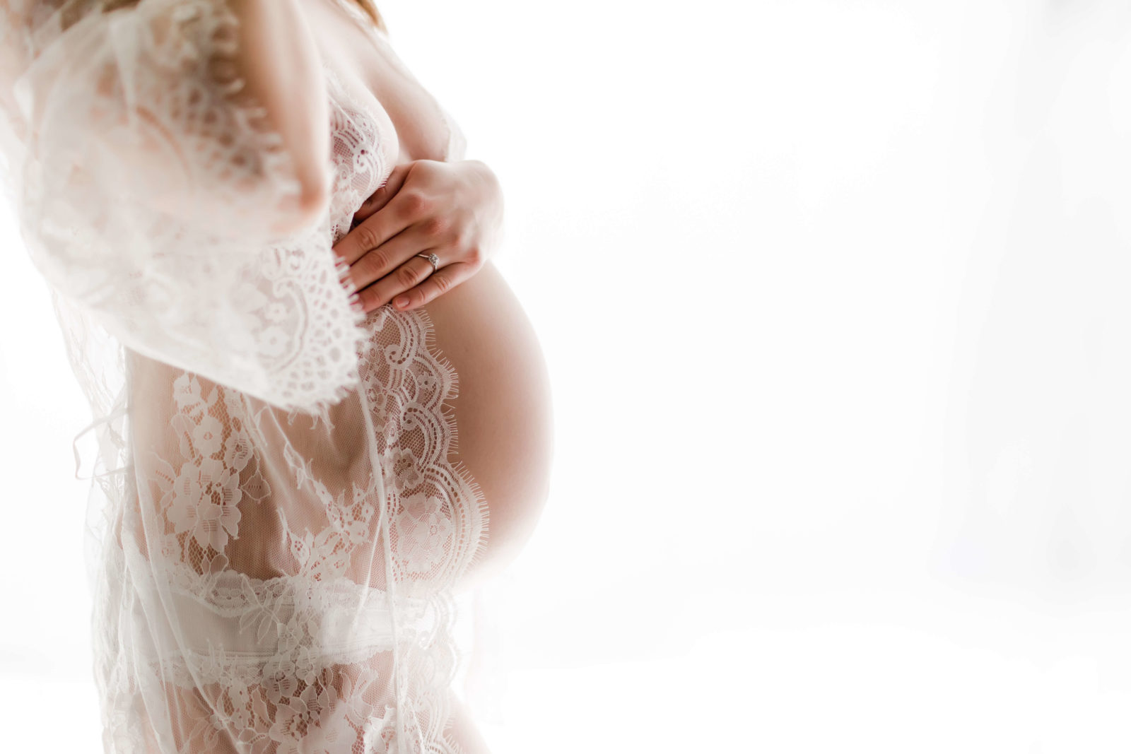 woman in lace robe holing on to pregnant belly during bare belly portraits