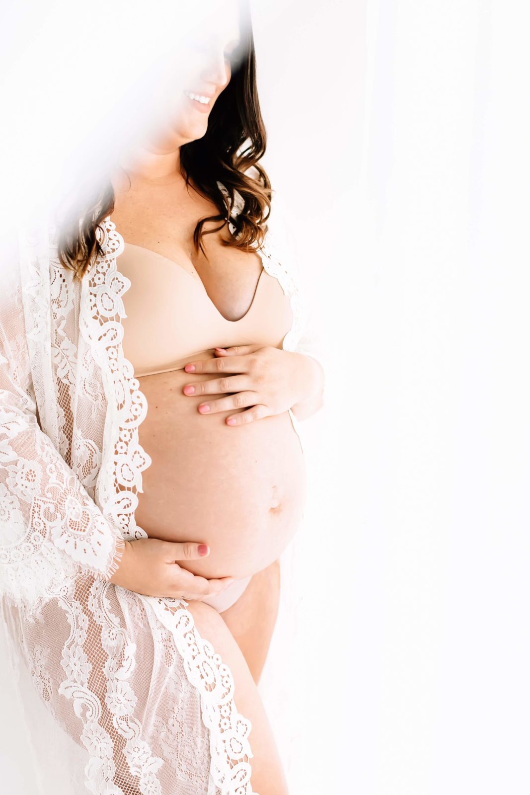 pregnant woman with pink nails curly hair and lace robe during bare belly session
