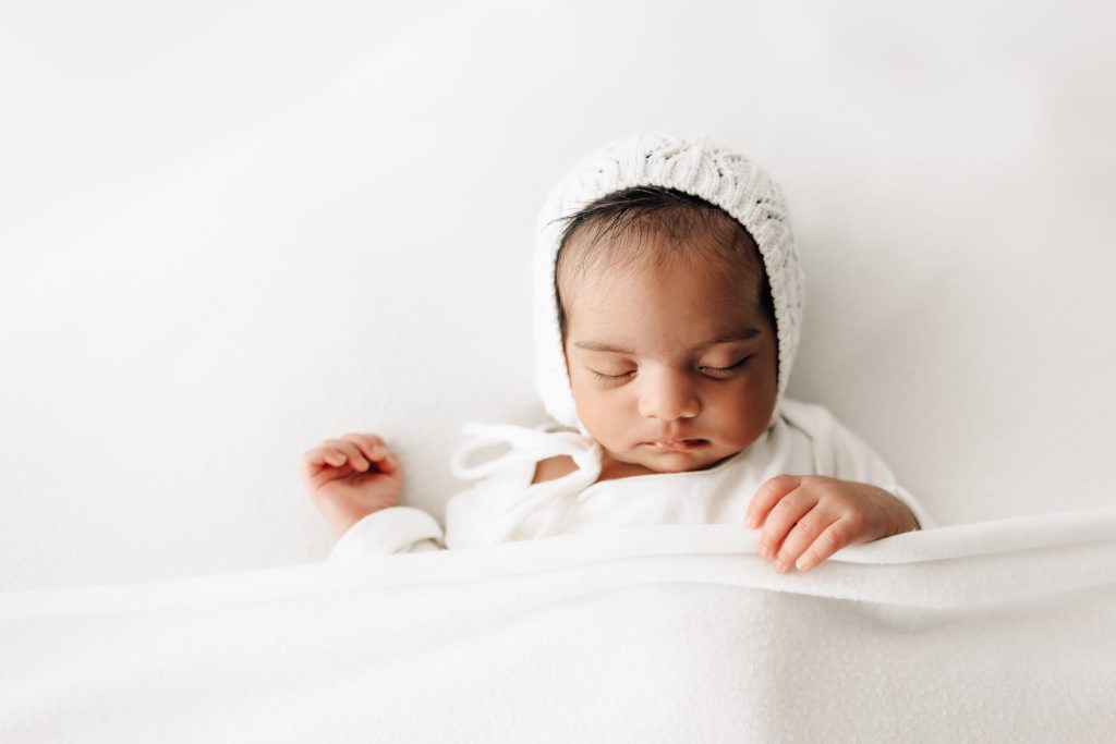 newborn baby in white bonnet and white blanket