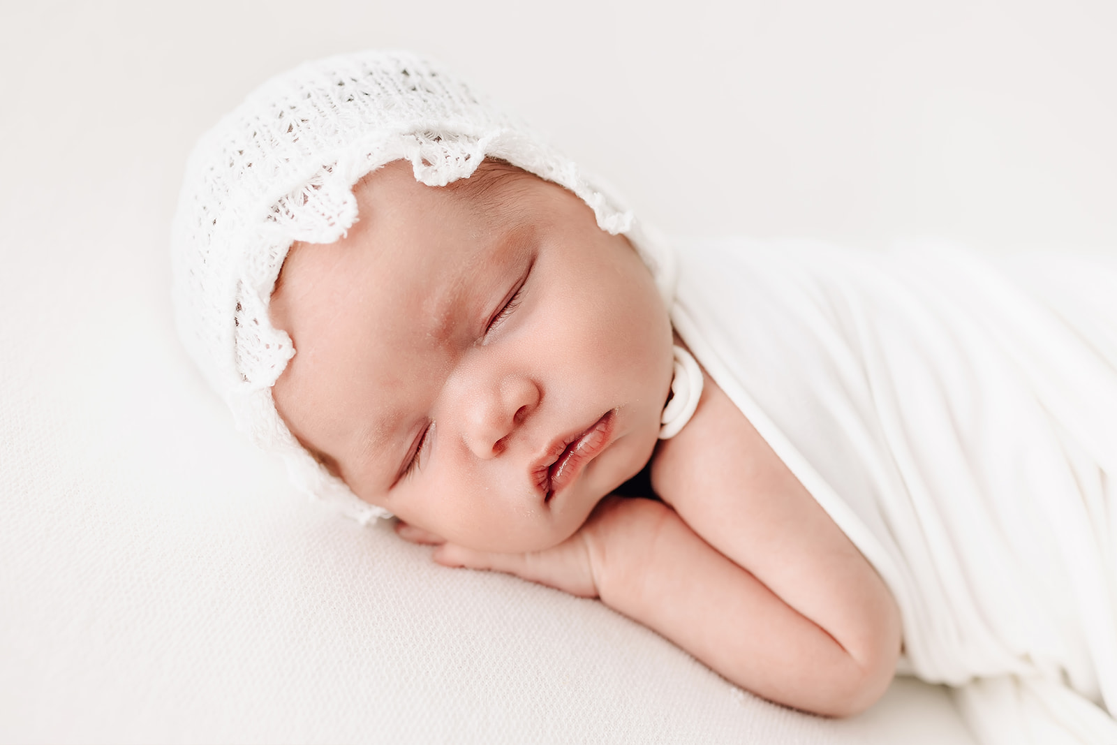 A newborn baby sleeps in a white bed on it's hands