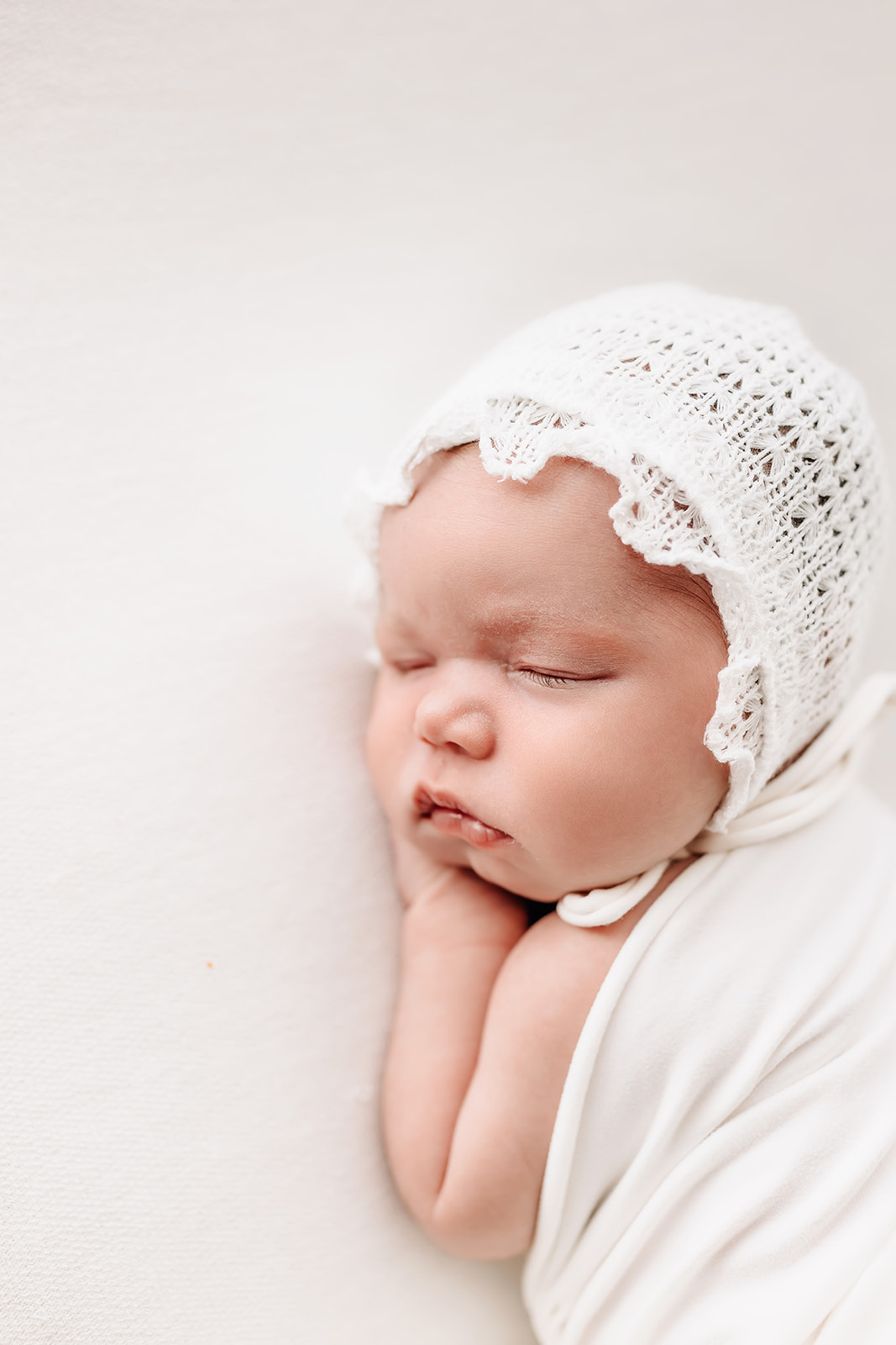 A newborn baby sleep on it's hands wearing a white lace bonnet City Sprouts