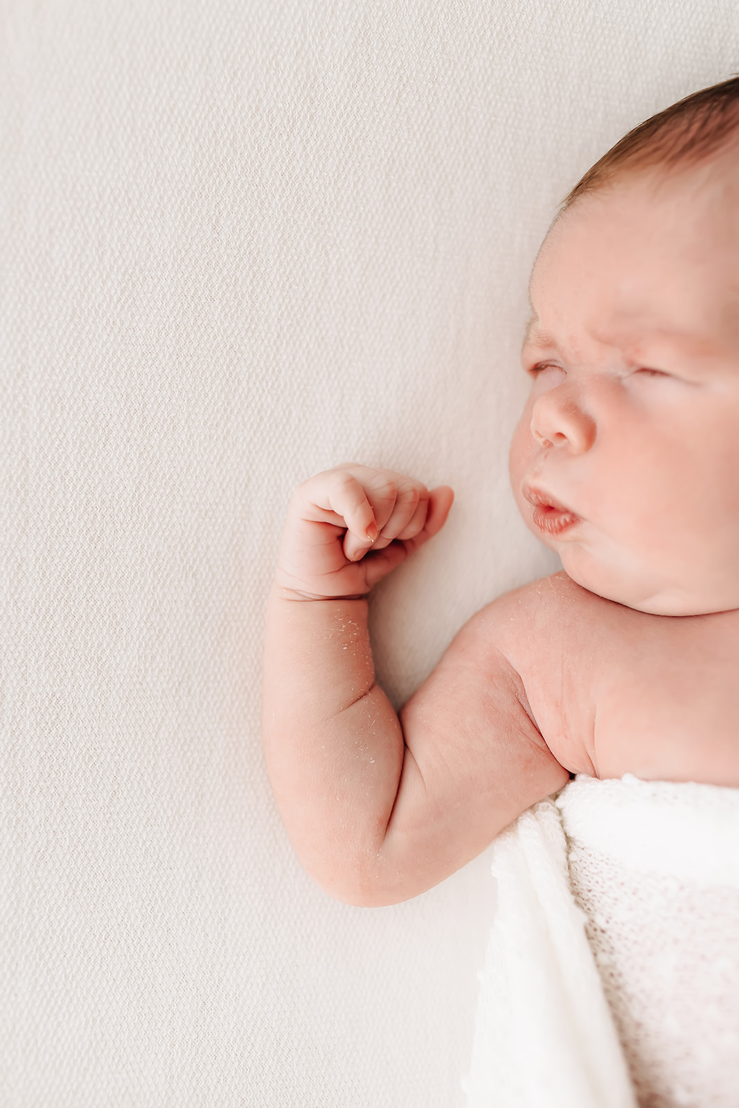 newborn baby sleeps on a bed with arm up like flexing muscles cotton babies saint louis