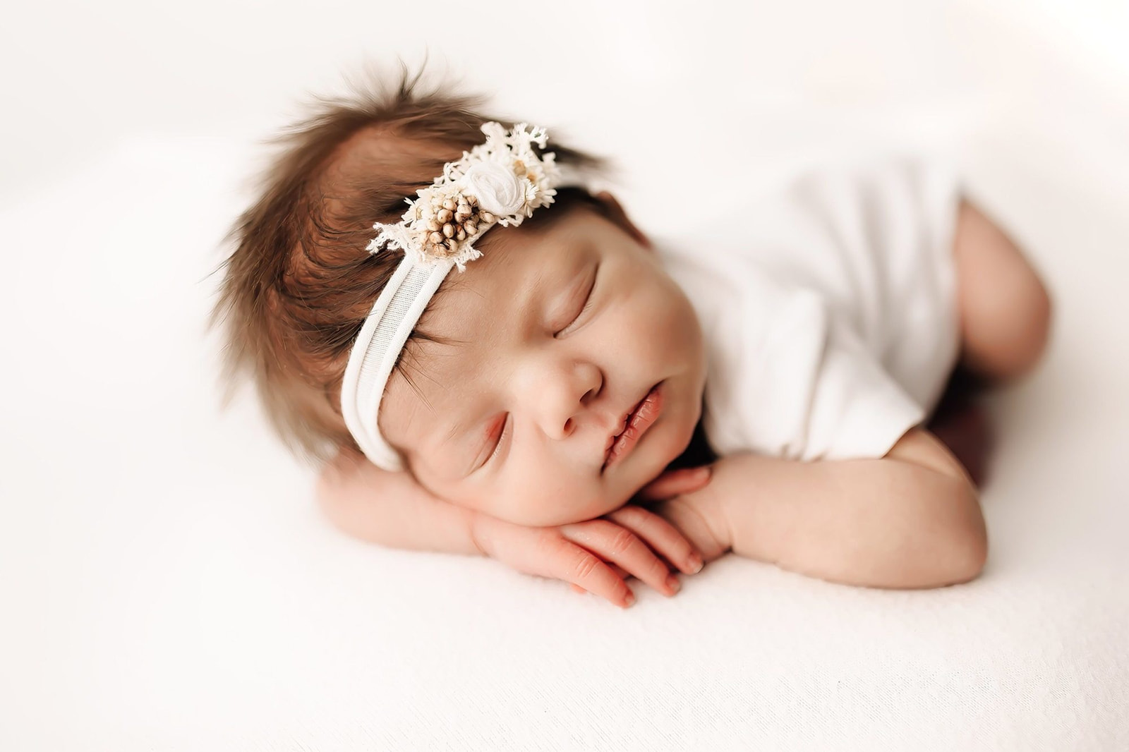 newborn baby sleeps in froggy pose with a white flower headband dancing for birth