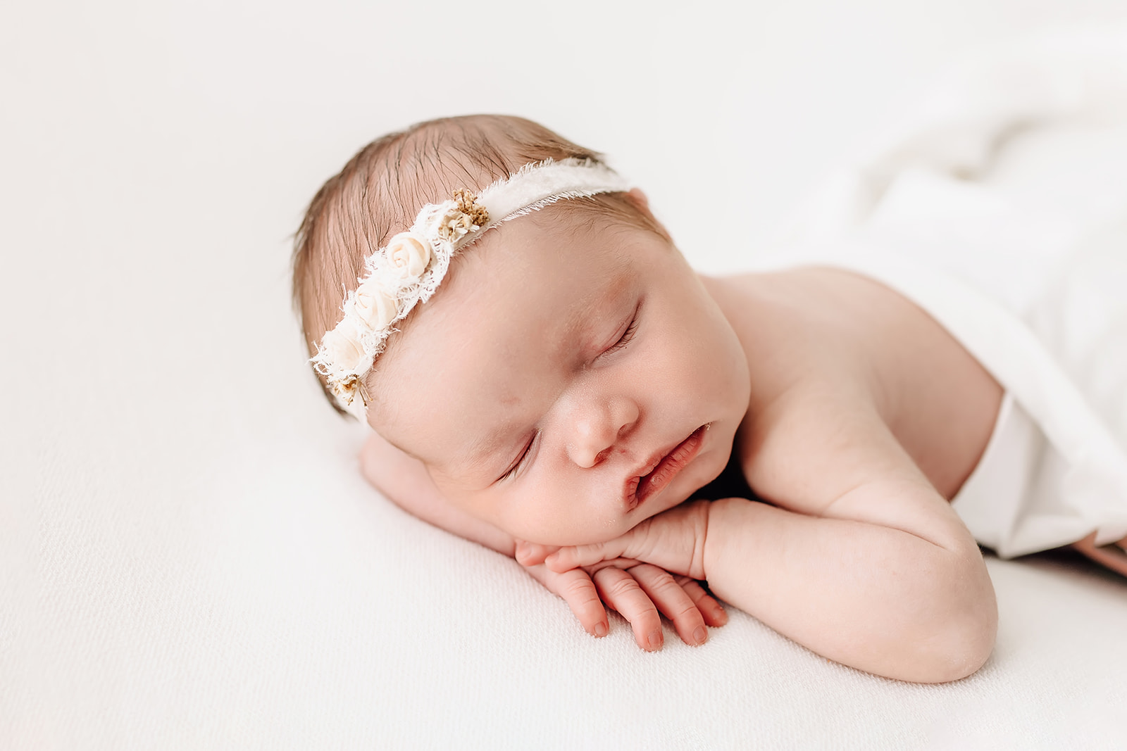 newborn baby sleeps on her hands wearing a white rose headband honeycomb st louis