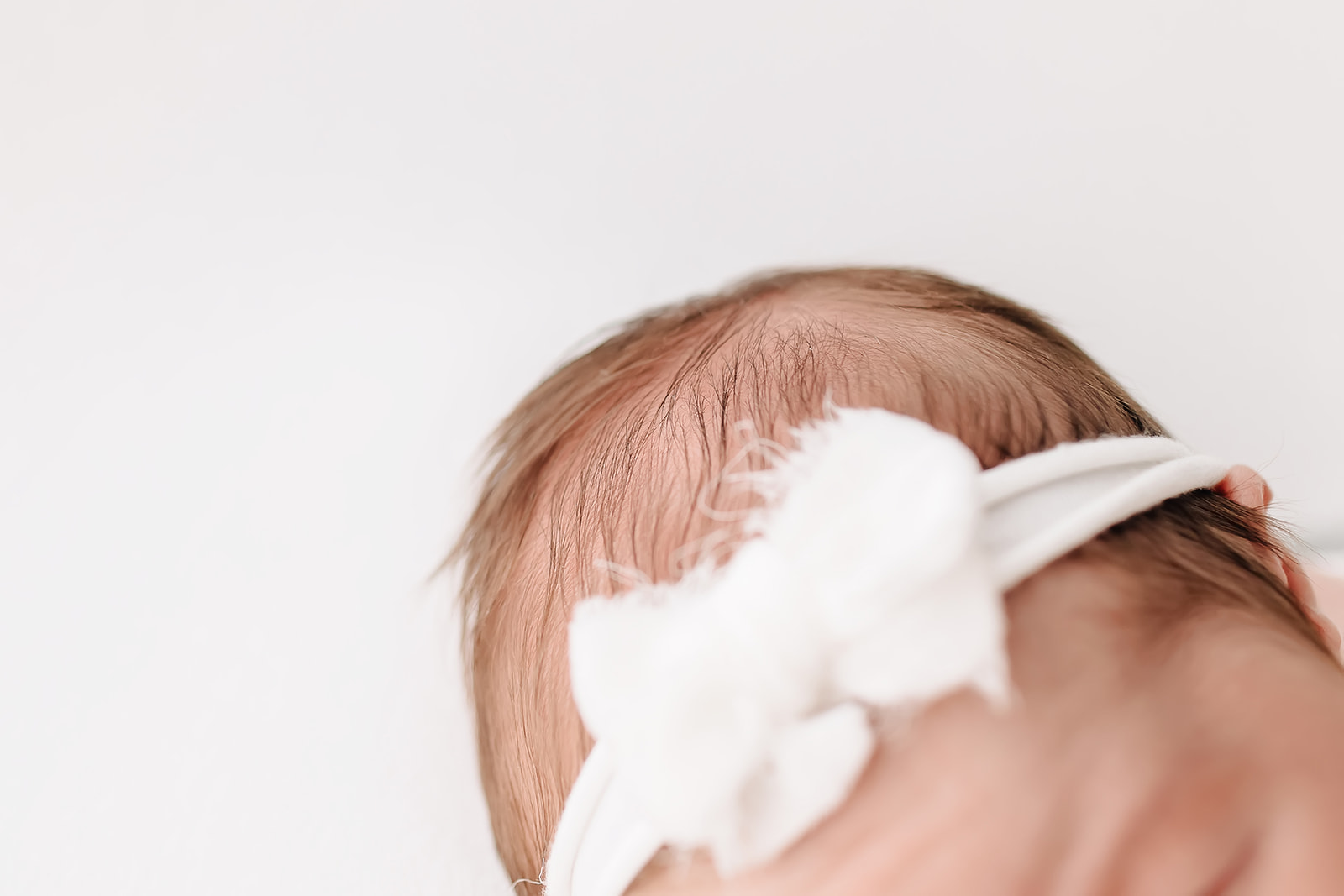 A newborn baby wears a white bow headband