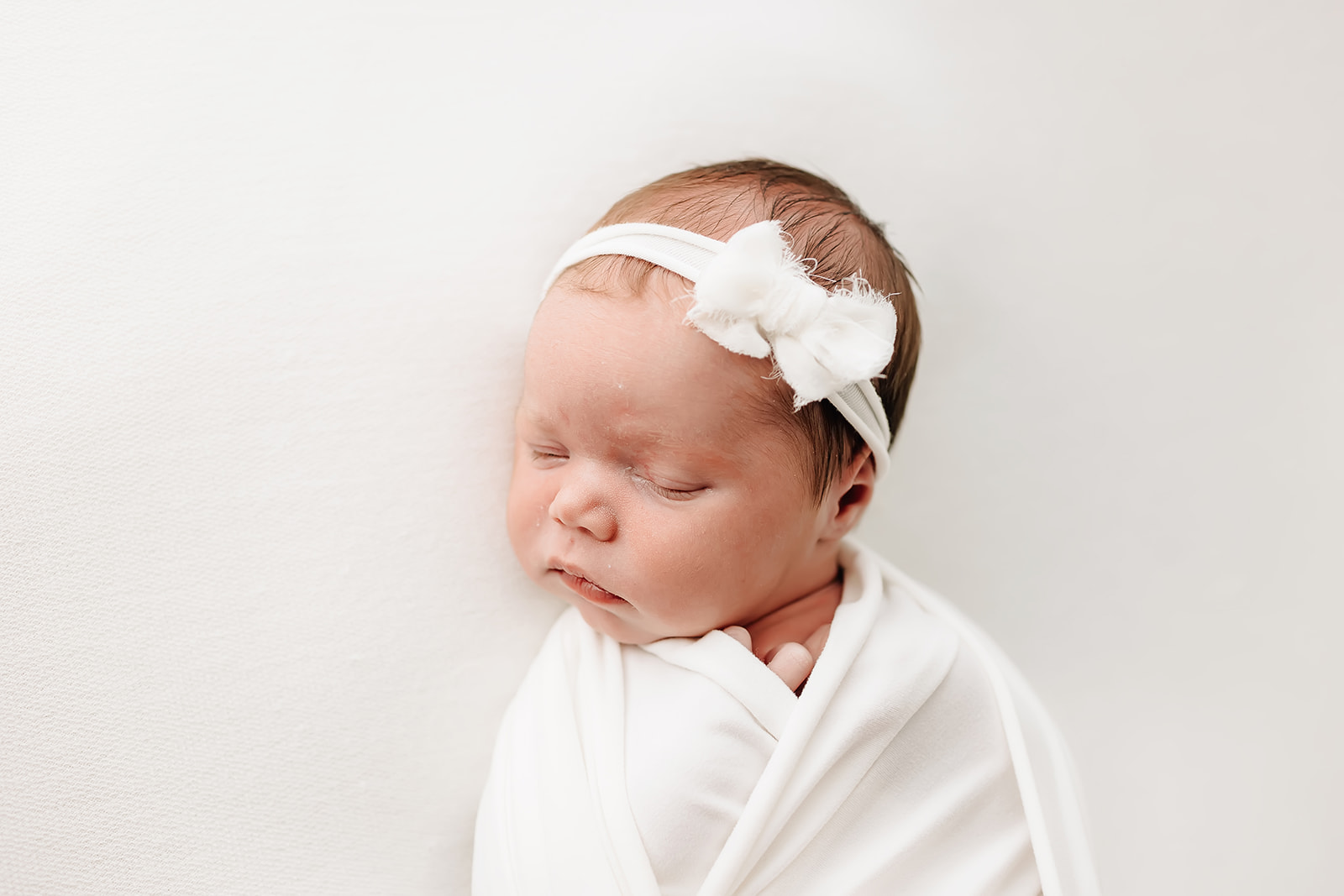 A newborn baby sleeps while wearing a white bow headband la leche league st louis