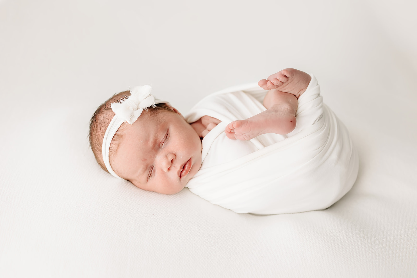 A newborn baby sleeps in a white swaddle with toes sticking out la leche league st louis