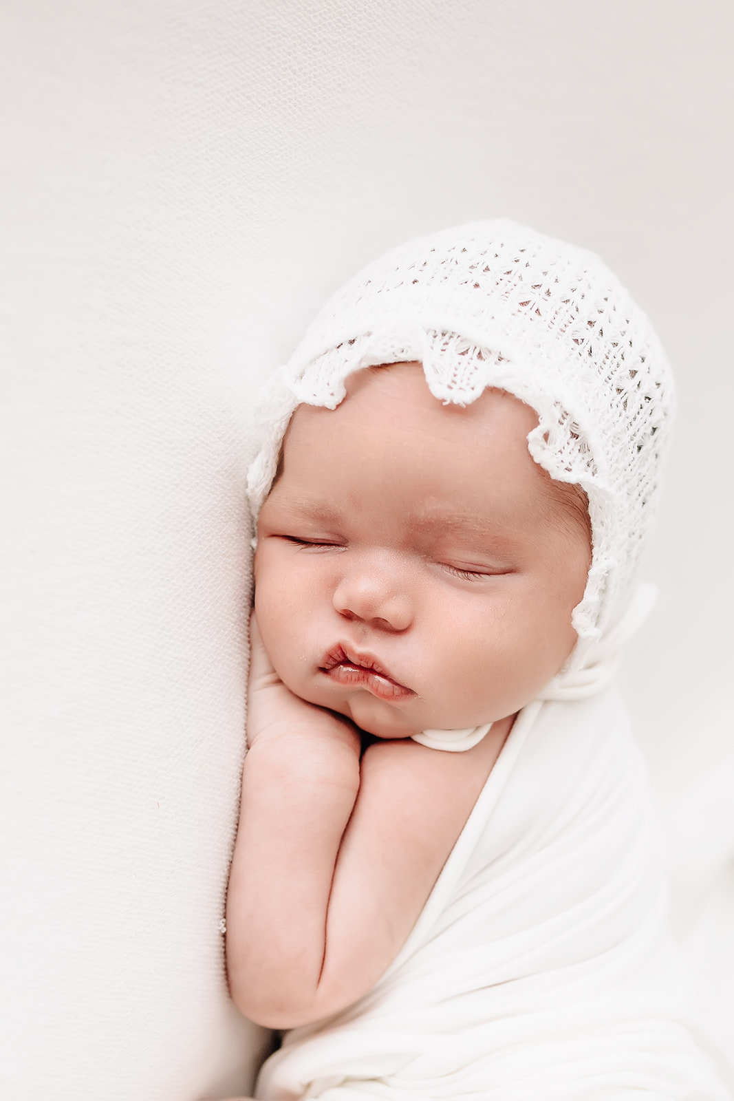 A newborn baby sleeps while wearing a white lace bonnet St Louis birth center