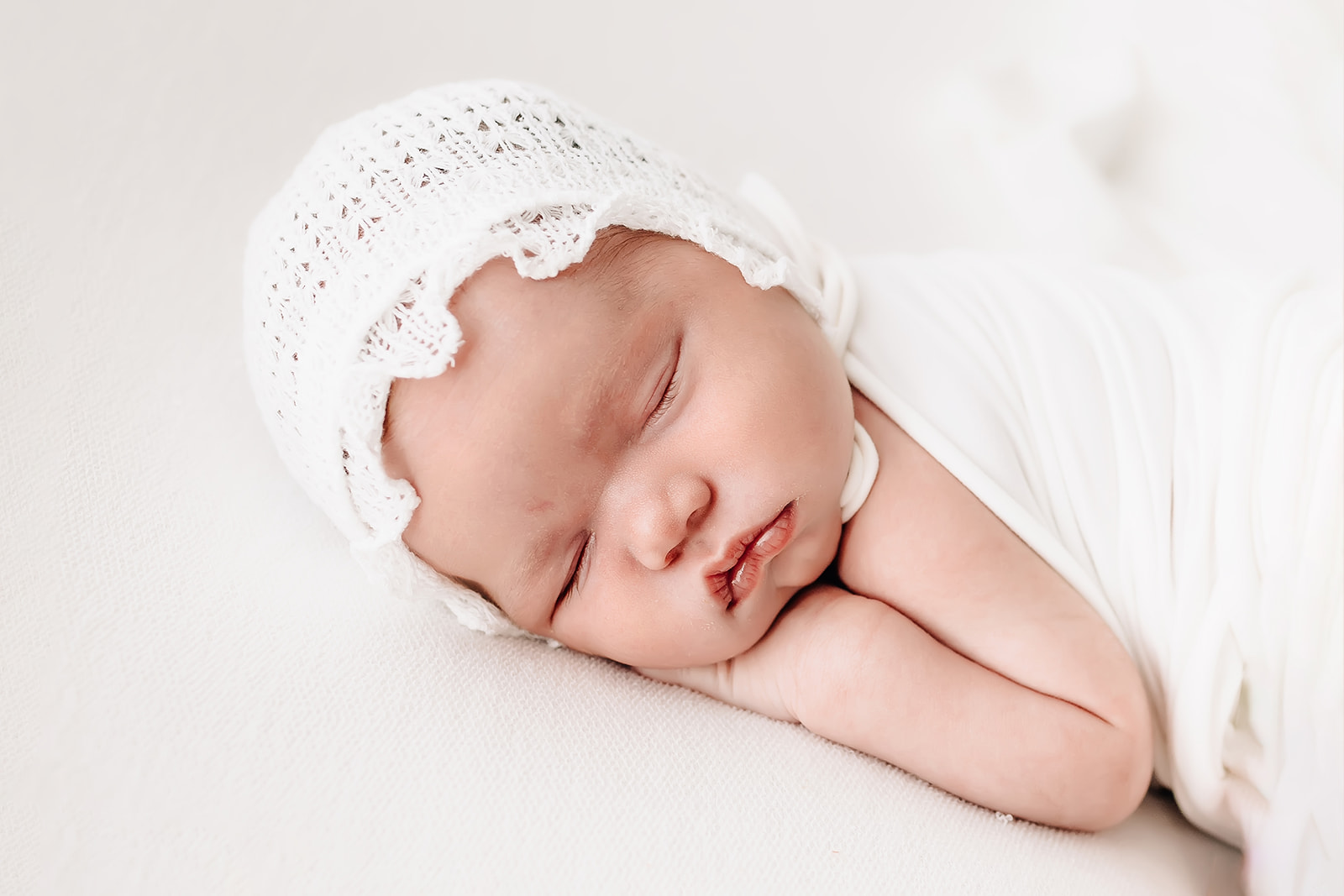 A newborn baby sleeps resting its head on its hands iin a white lace bonnet St Louis birth center