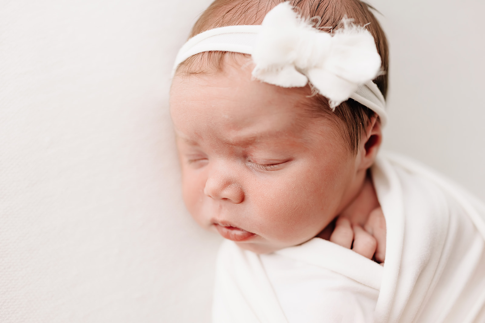 A newborn baby sleeps in a white boy headband