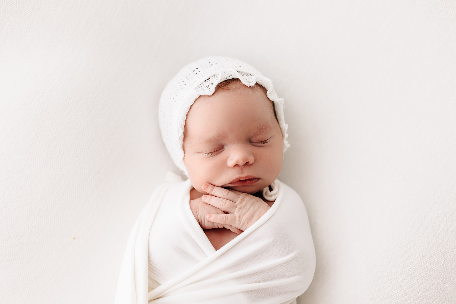 A newborn baby sleep in a white swaddle and bonnet St Louis prenatal yoga