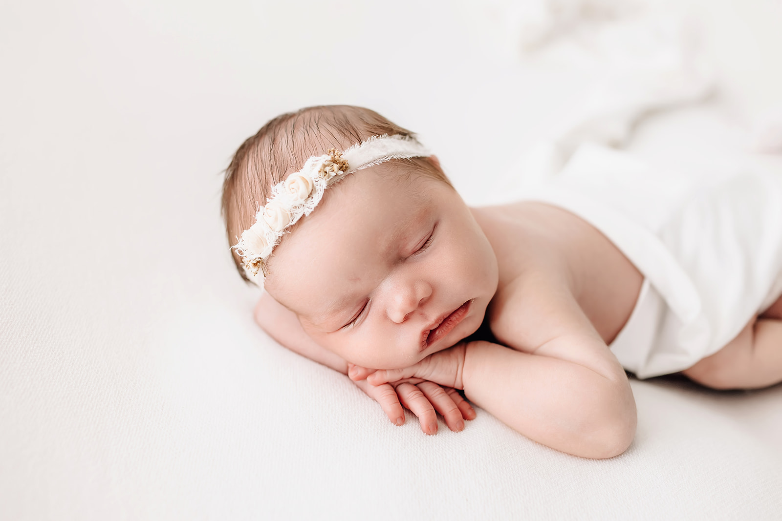 A newborn baby sleeps resting its head on its hands under a white blanket lake st louis pediatricians