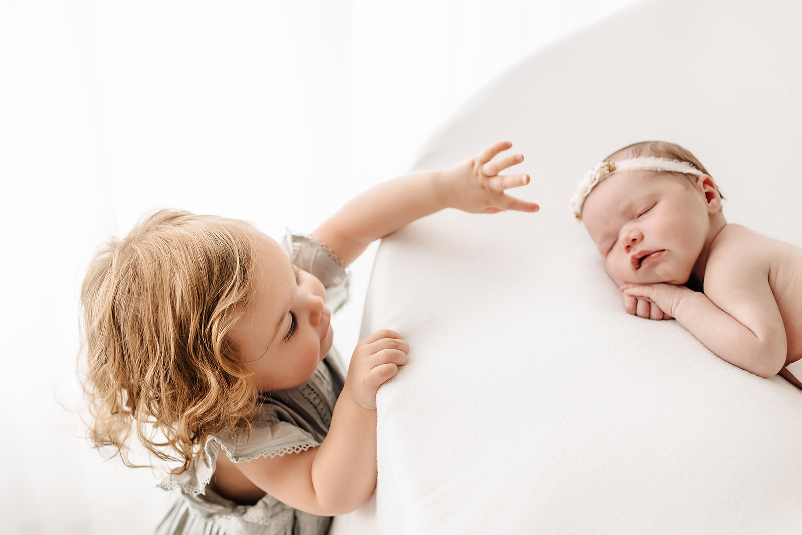 A young girl reaches up to a touch her sleeping newborn baby sibling lake st louis pediatricians