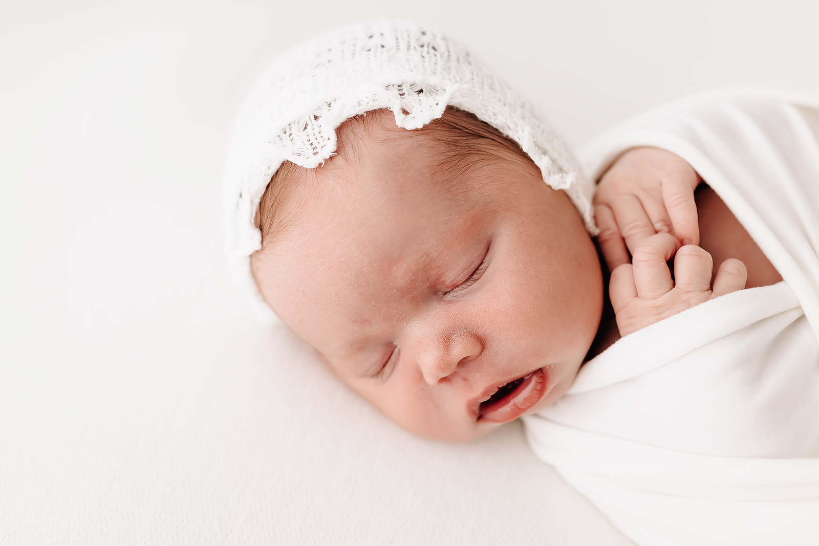 Details of a sleeping newborn baby in white bonnet