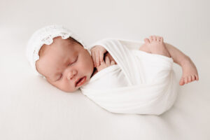 A newborn baby wrapped in a white swaddle sleeps with toes hanging out Mercy Hospital Maternity Ward