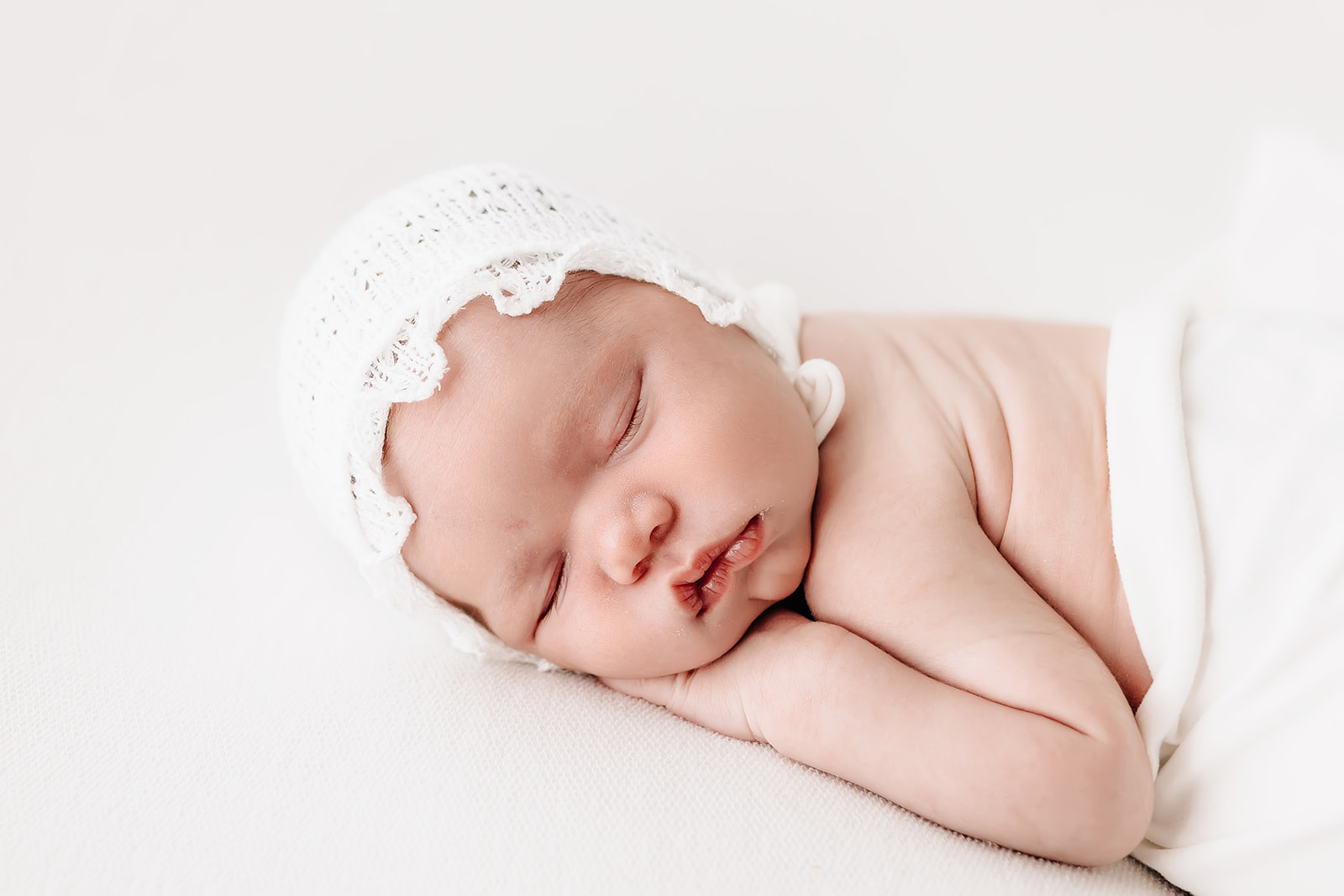 A newborn baby sleeps on its' hands while wearing a white lace bonnet Mercy Hospital Maternity Ward