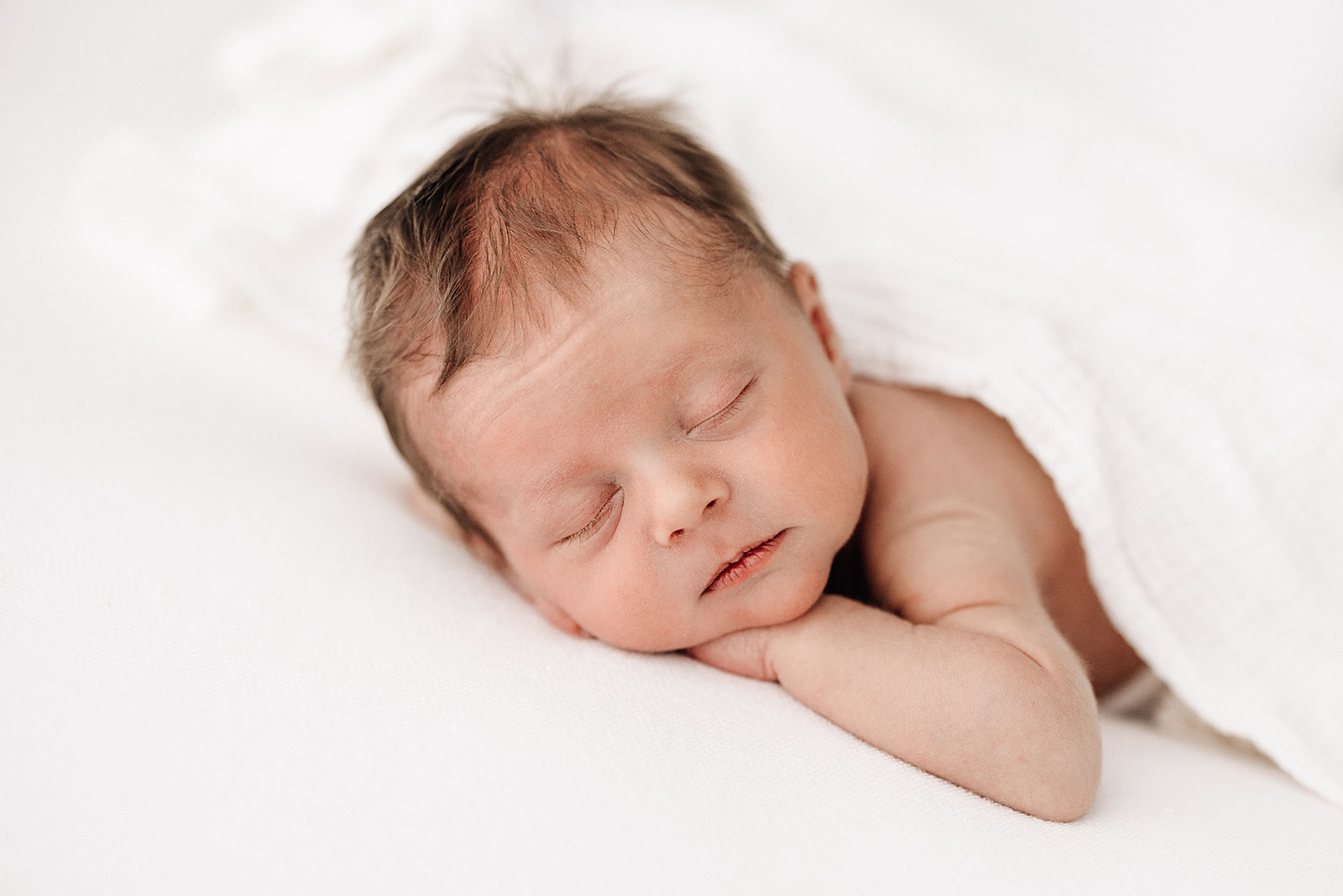 A newborn baby sleeps with its chin on its hand