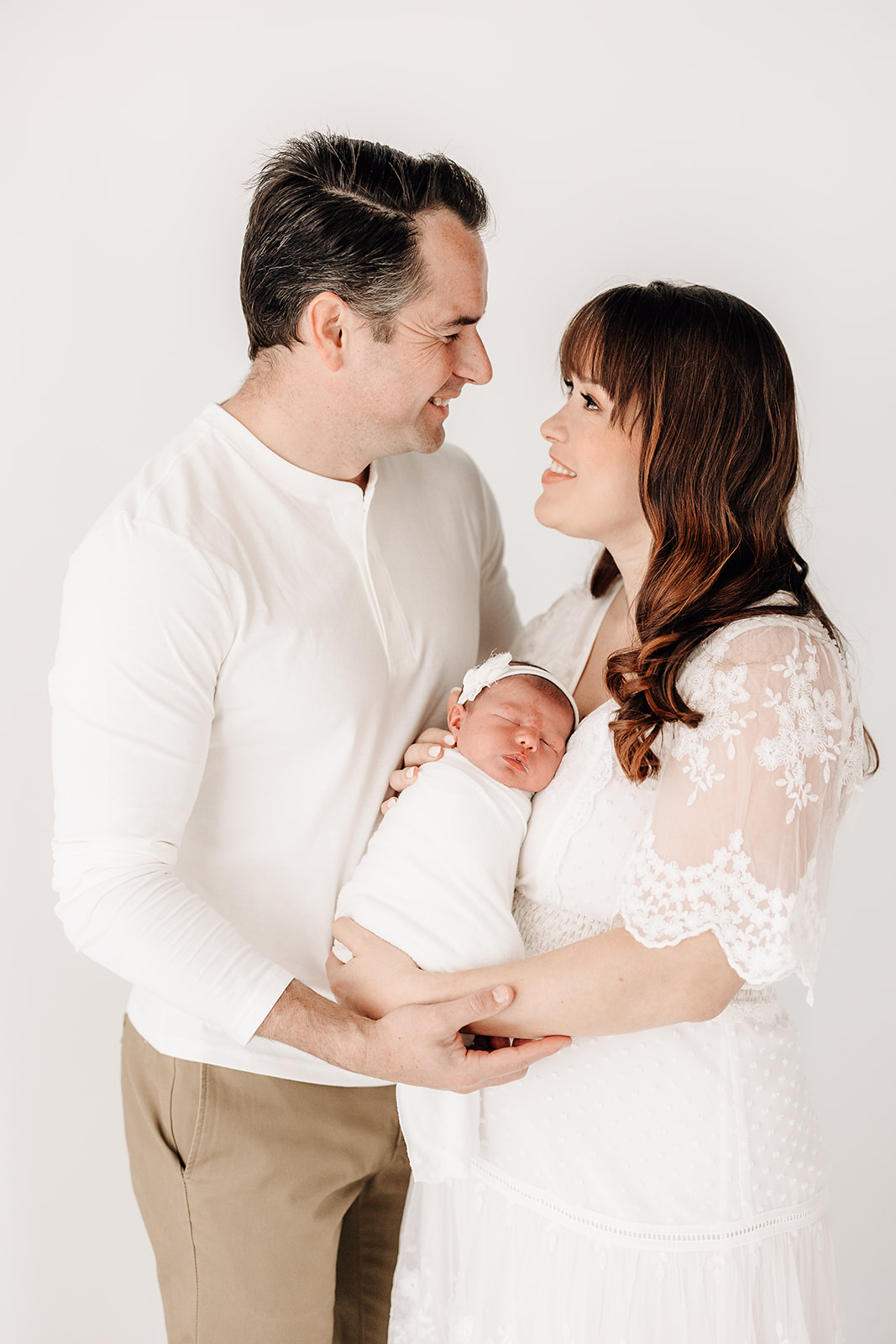New parents stand together cradling their newborn baby daughter in a studio