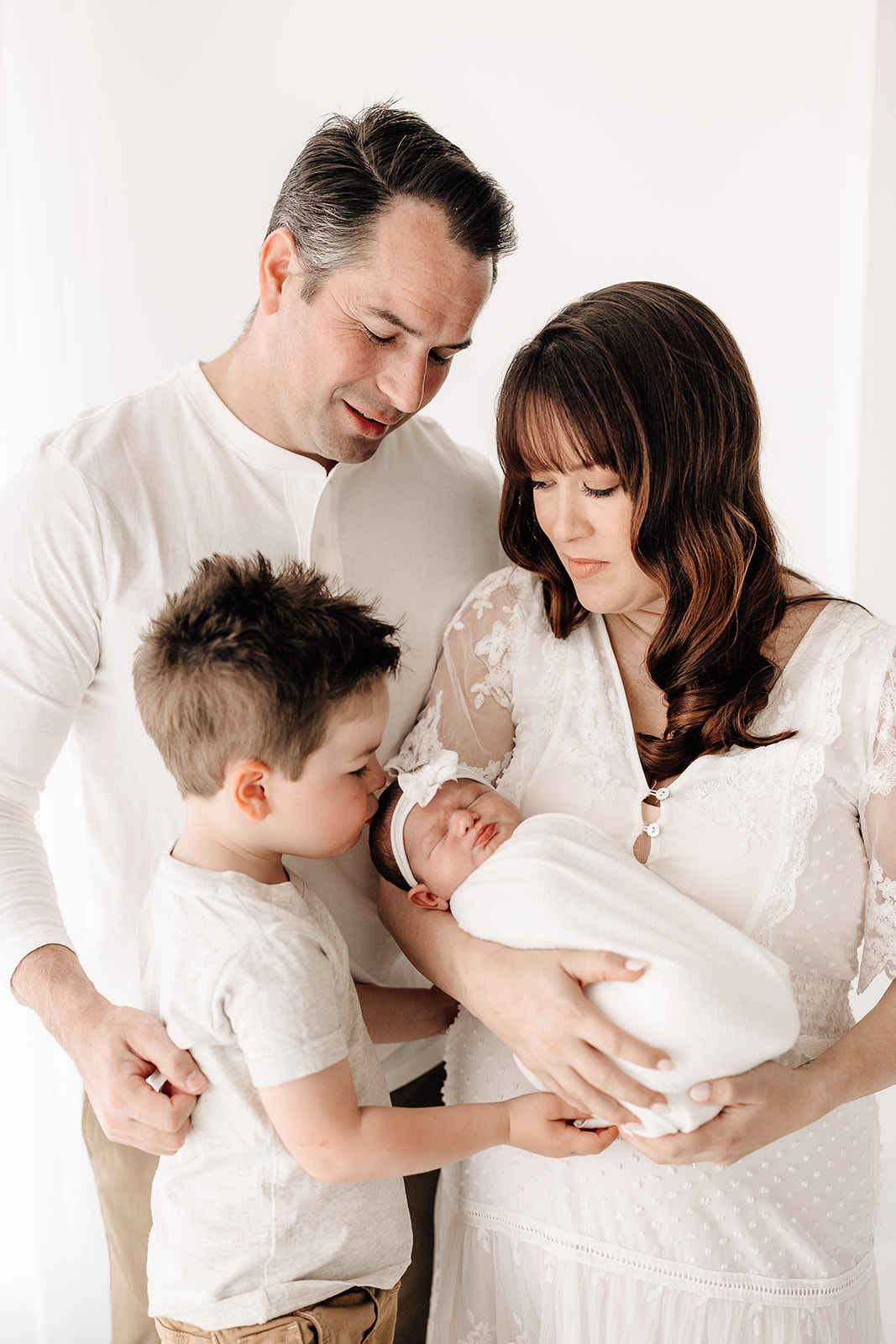 A mother holds her newborn baby daughter while her older son kisses her and dad leans in St. Louis Nannies