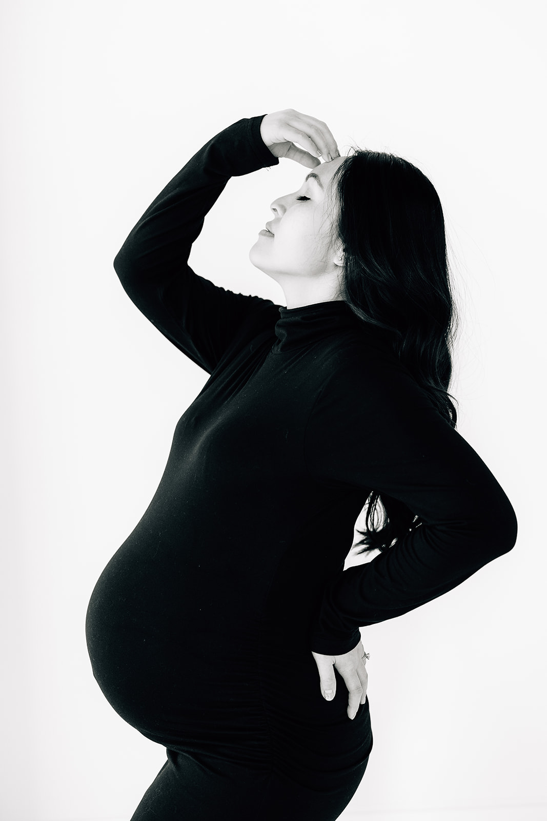 A mom to be stands in a studio wearing a black maternity gown with a hand on her forehead Birthing classes St. Louis