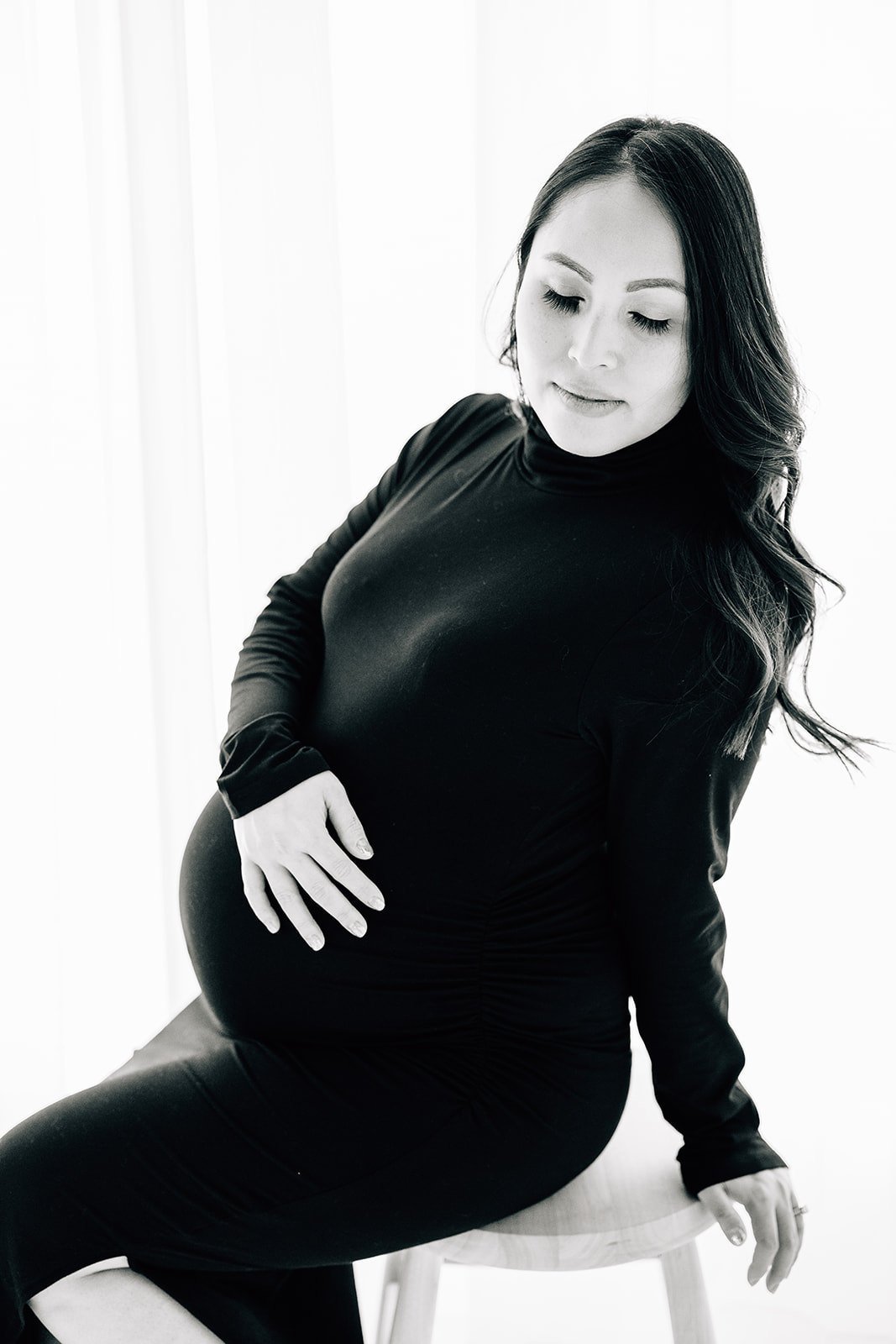 A mom in a black maternity gown sits on a stool looking down her shoulder Birthing classes St. Louis