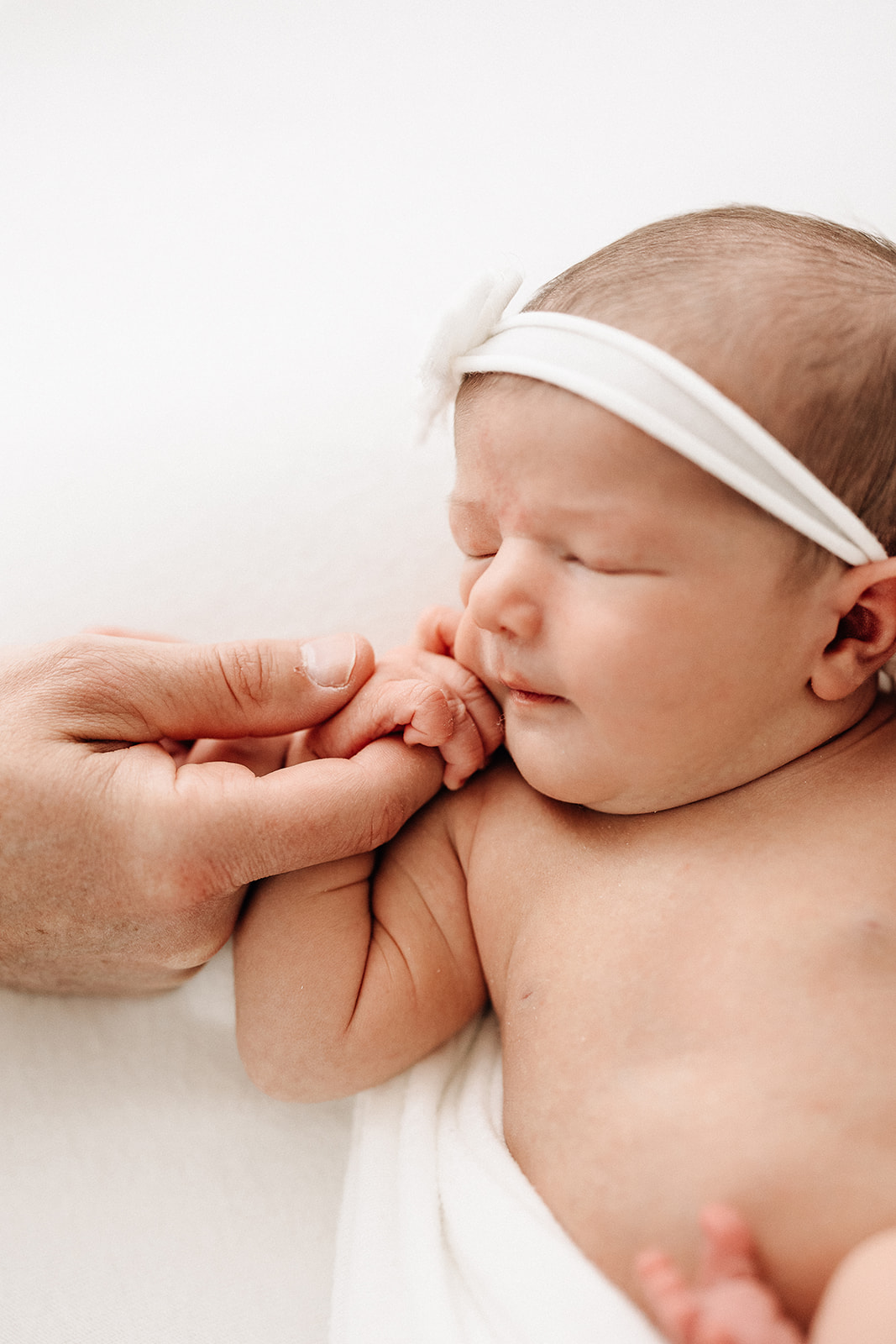 Details of a newborn baby holding dad's finger while laying on a white bed