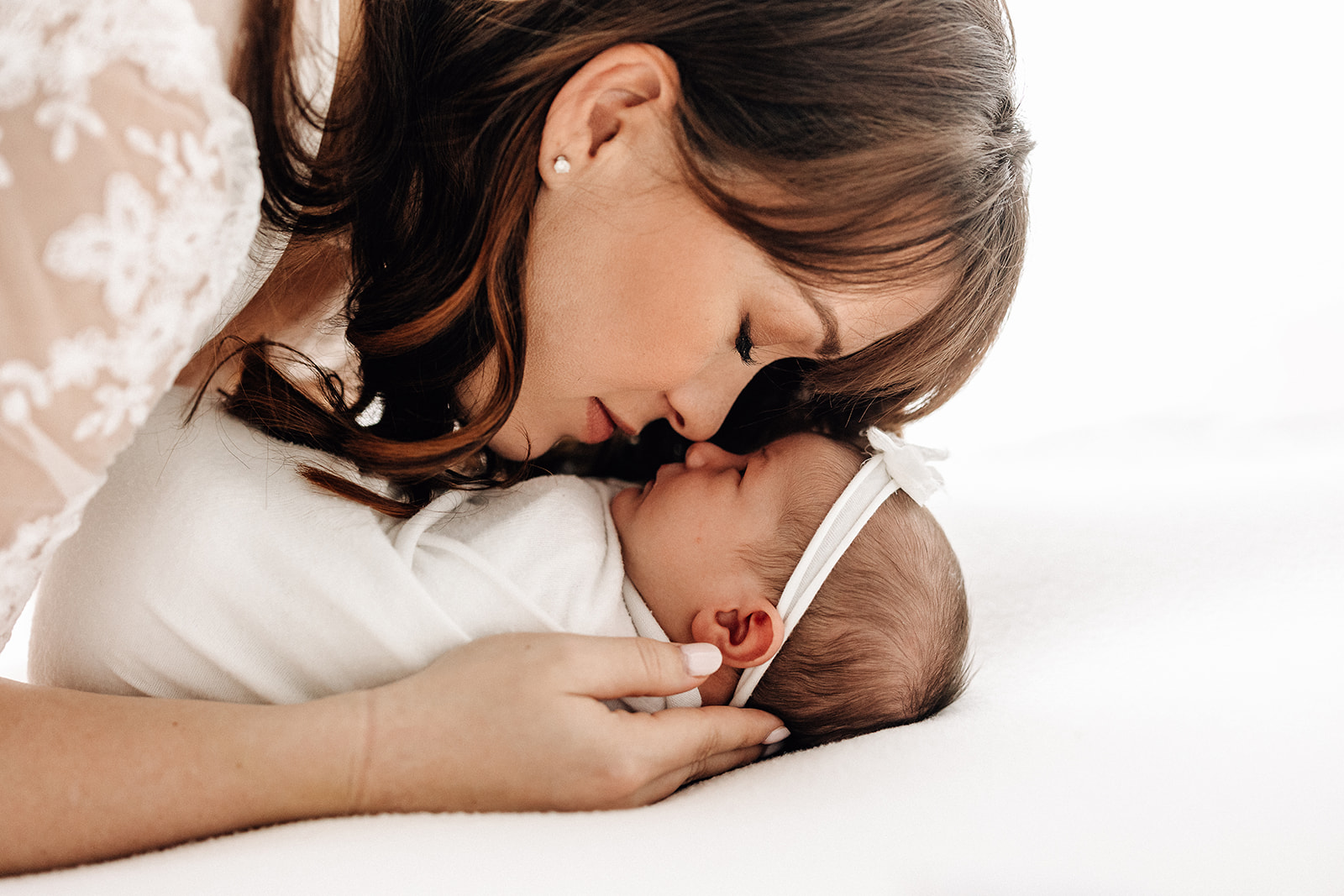 A new mom nuzzles nose to nose with her newborn baby daughter on a white bed Barefoot Midwife