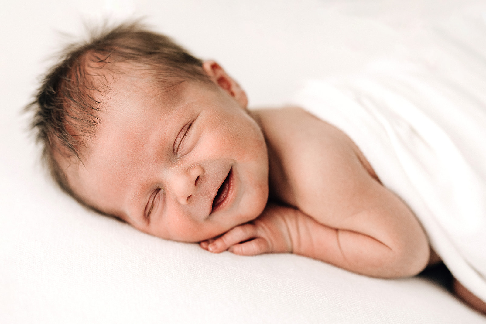 A newborn baby smiles in its sleep on a white bed with help from a lactation consultant St. Louis