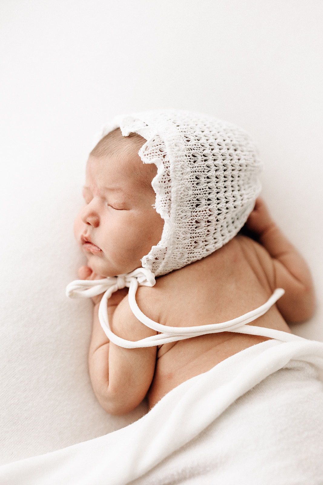 A newborn baby in a white knit bonnet sleeps on her stomach before visiting St. Louis Pediatricians