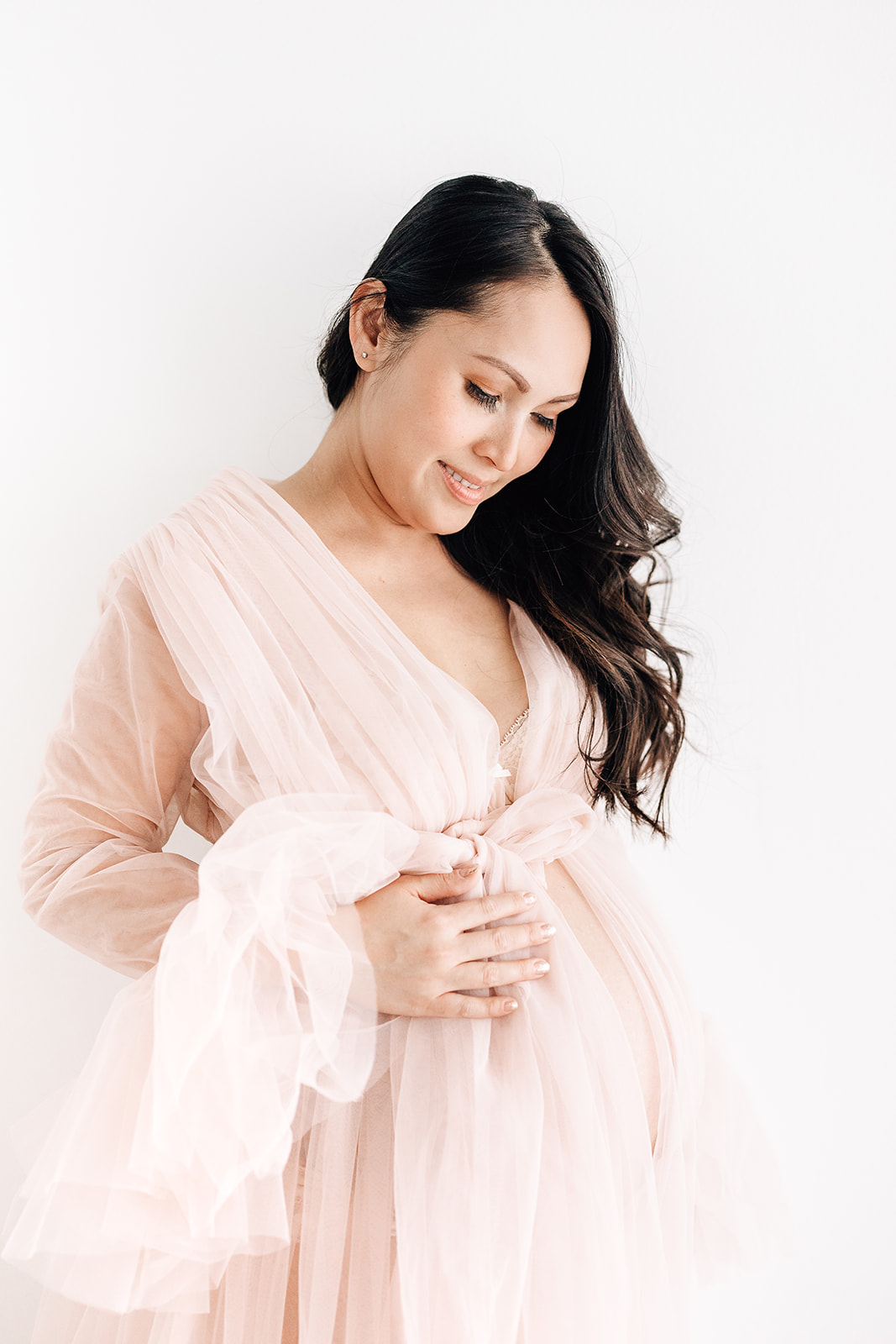 A mother to be in a pink maternity gown open on the belly smiles down to her bump