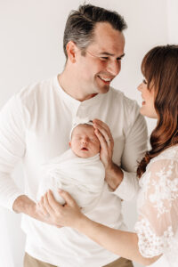 A happy father holds his sleeping newborn baby daughter with mom in a studio after some Parenting Classes St. Louis