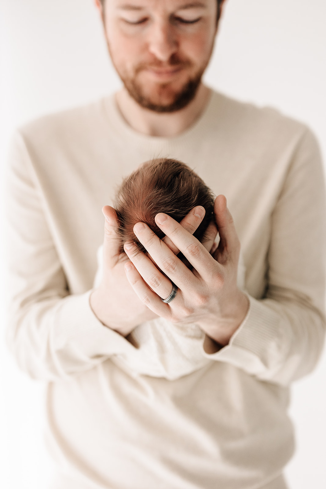 A father holds his sleeping newborn baby out in front of him while standing in a studio