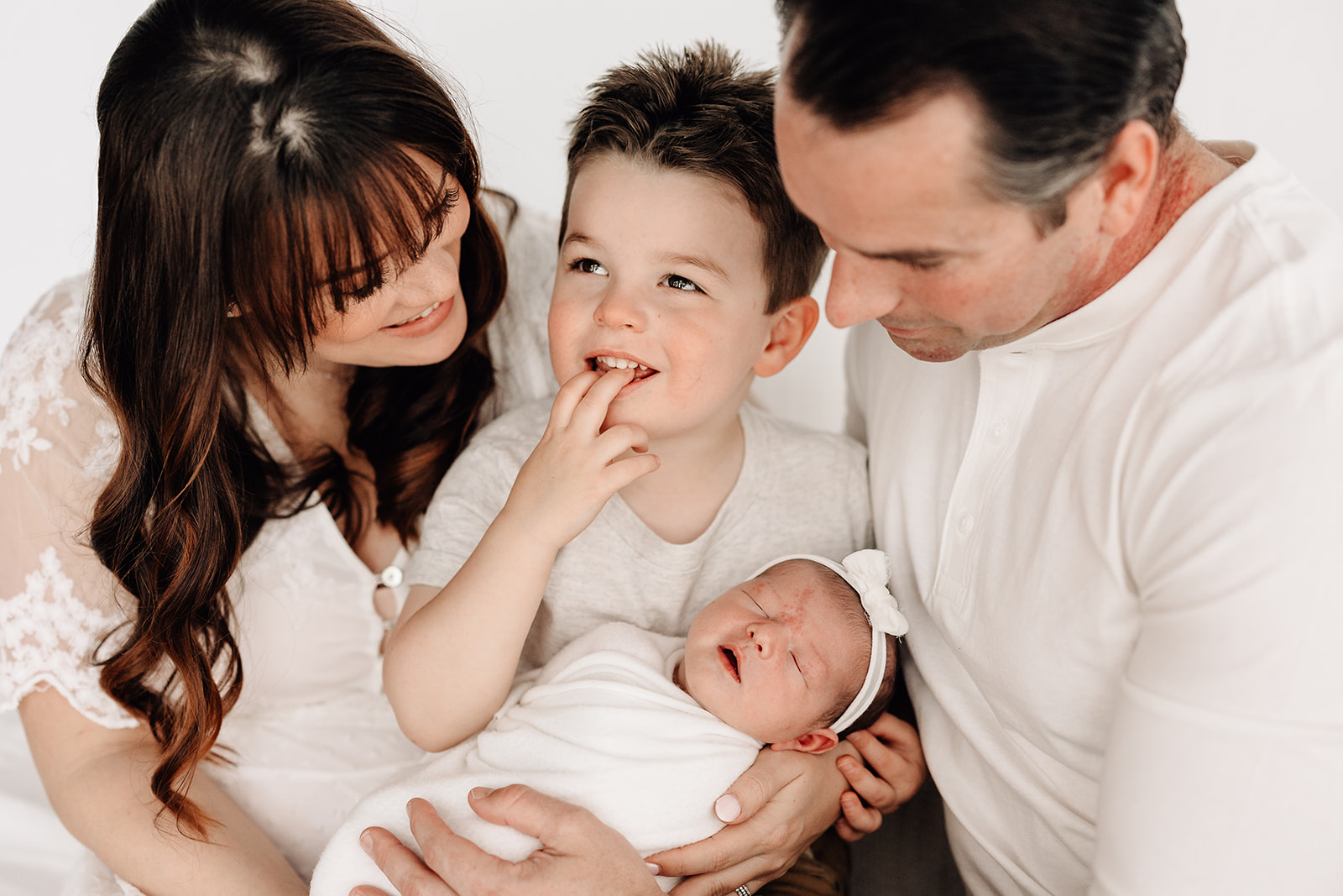 A mom and dad sit in a studio holding their sleeping newborn baby with their toddler son before visiting playgrounds St. Louis