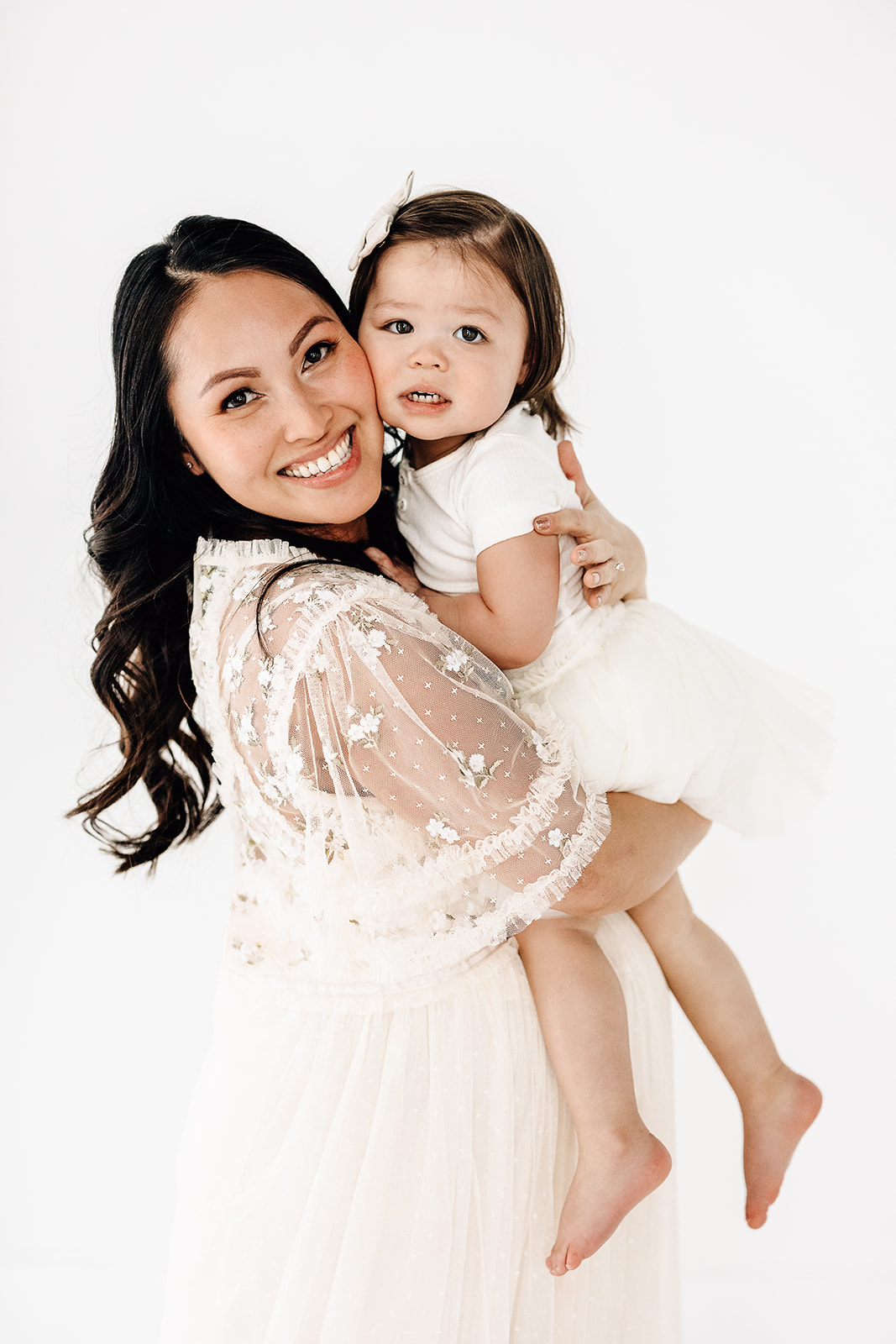 A happy pregnant mother smiles with her toddler daughter while both wear white dresses after visiting Preschools in St. Louis