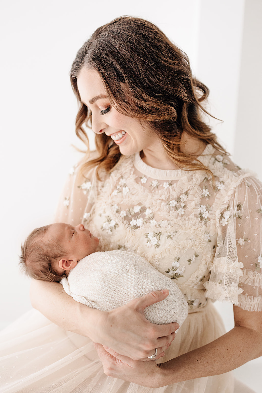 A smiling mom sits in a studio cradling her sleeping newborn in her arms