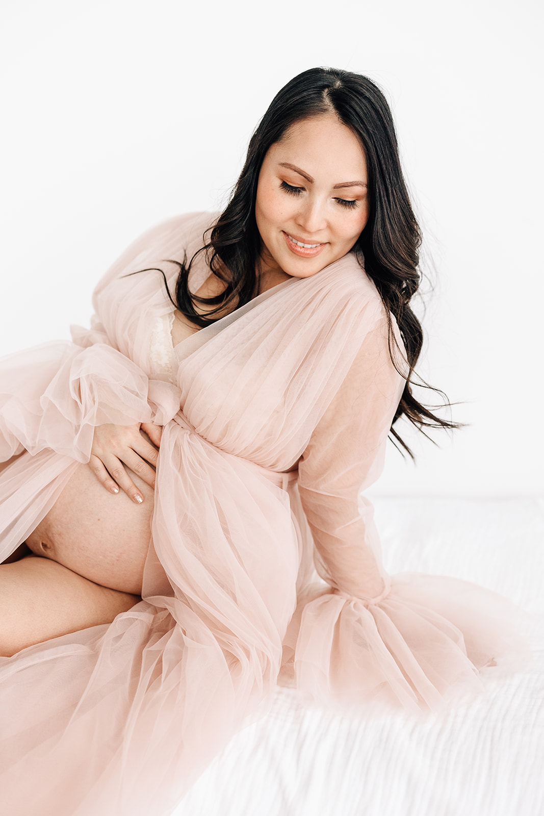 A mom to be smiles while sitting across a bed in an open pink tule maternity gown after visiting Jamaa Birth Village