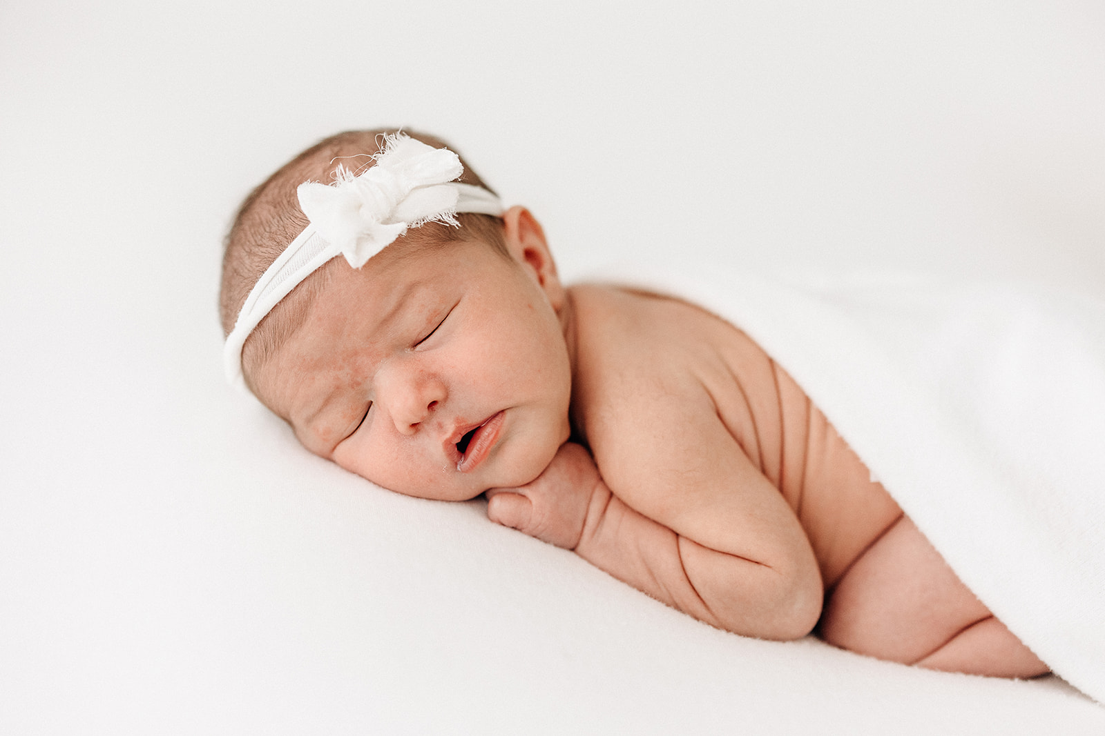 A newborn baby sleeps under a white blanket with a white headband thanks to STL Sitter