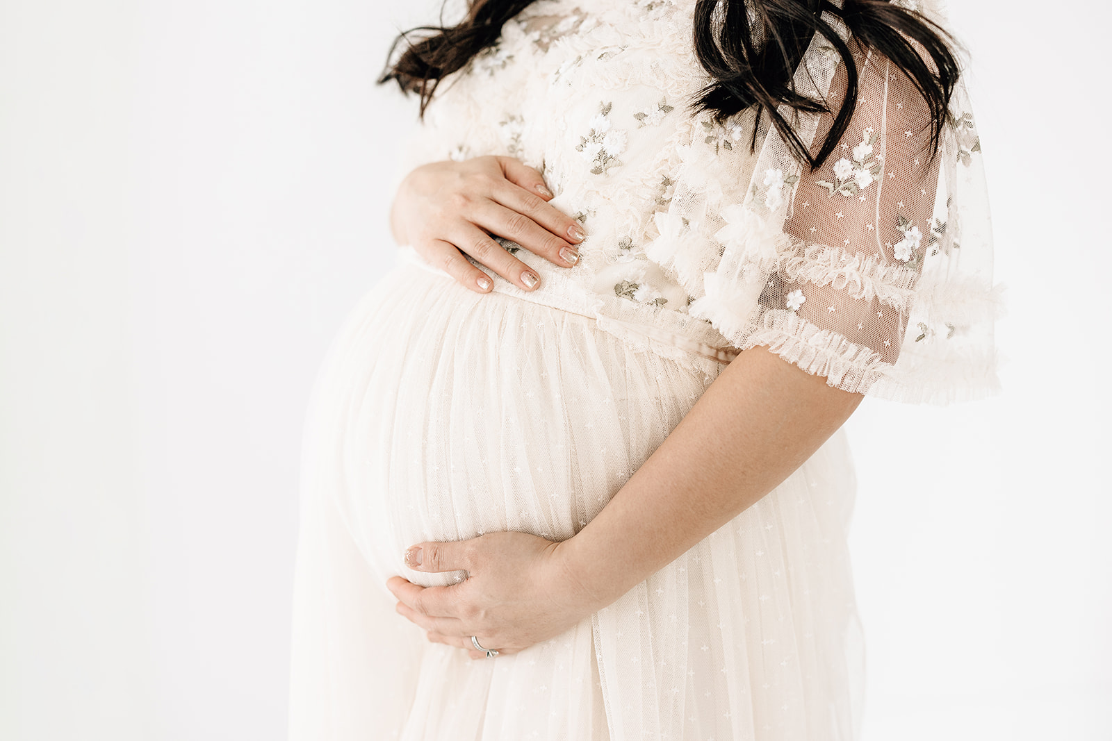 Details of a mother's bump as she holds it in a white maternity gown