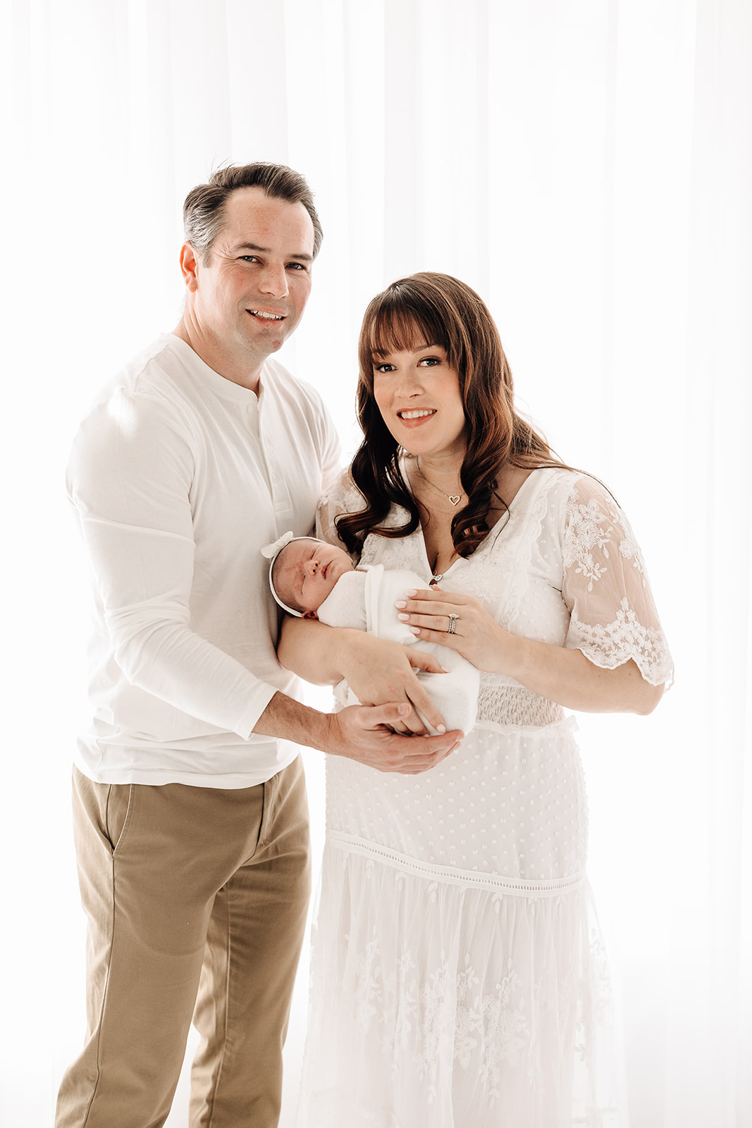 Happy new parents stand in a studio holding their sleeping newborn baby before meeting with Midwest Placenta Encapsulation