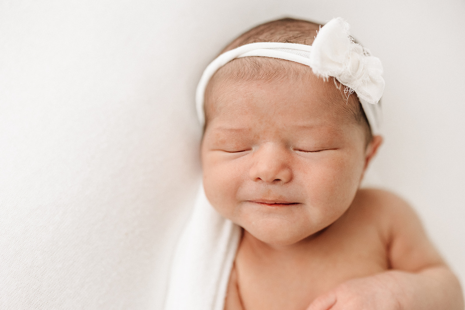 A newborn baby sleeps on a white bed with a white headband thanks to Moose Caboose