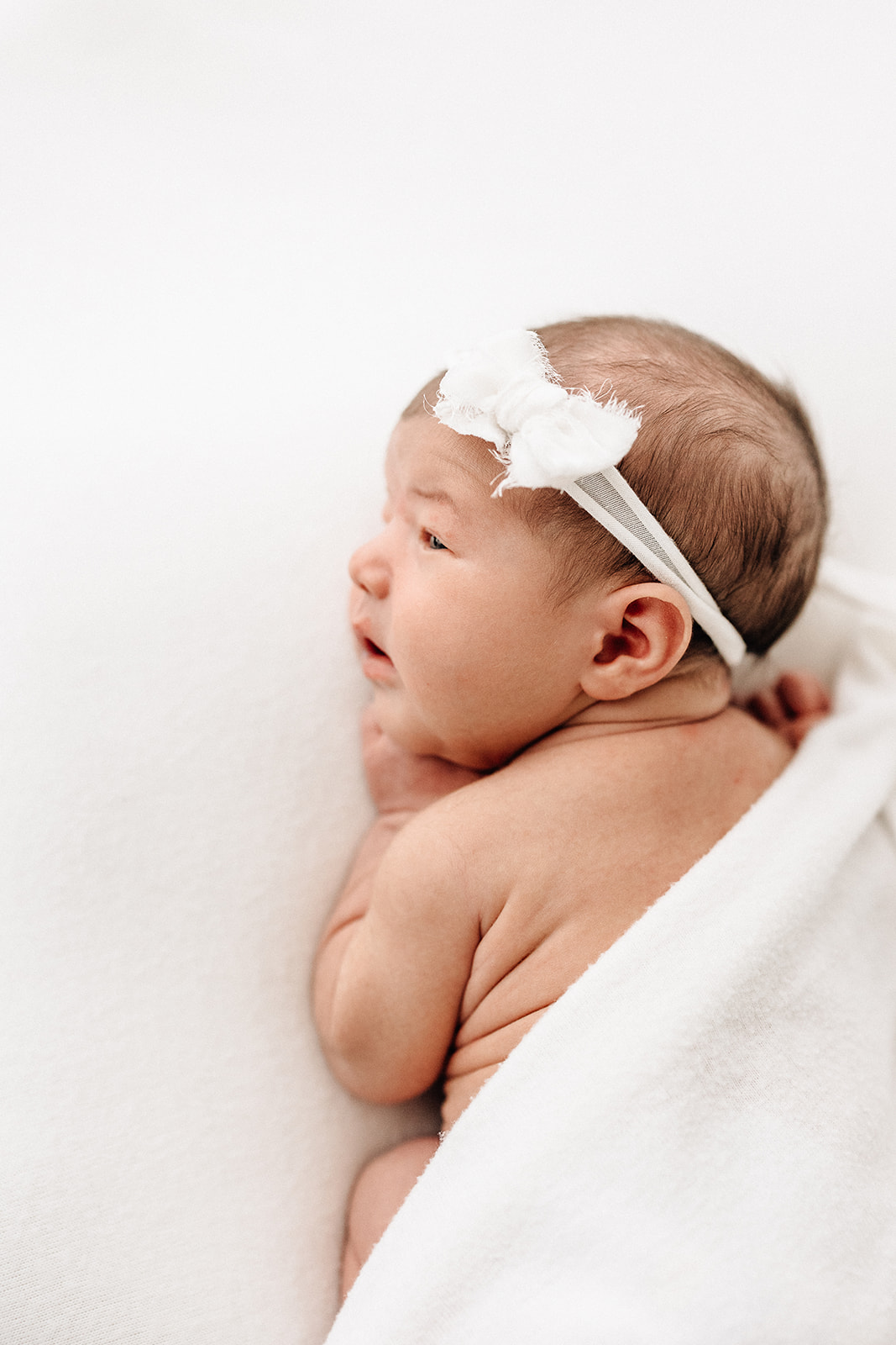 A newborn baby lays on a bed in froggy pose with eyes open after using Robbins doula services