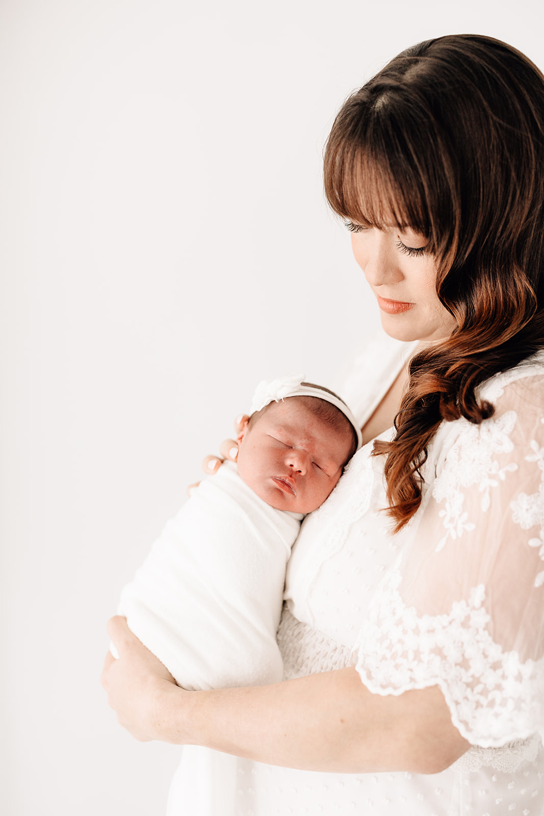 A newborn baby sleeps against mom's chest while standing in a studio