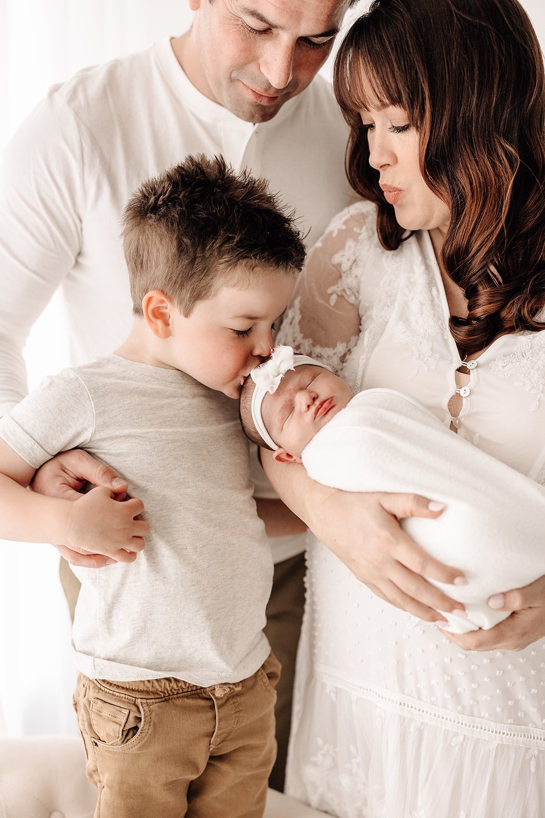 A toddler boy kisses the head of his newborn baby sister in mom's arms after meeting Star Of The Sea Doula