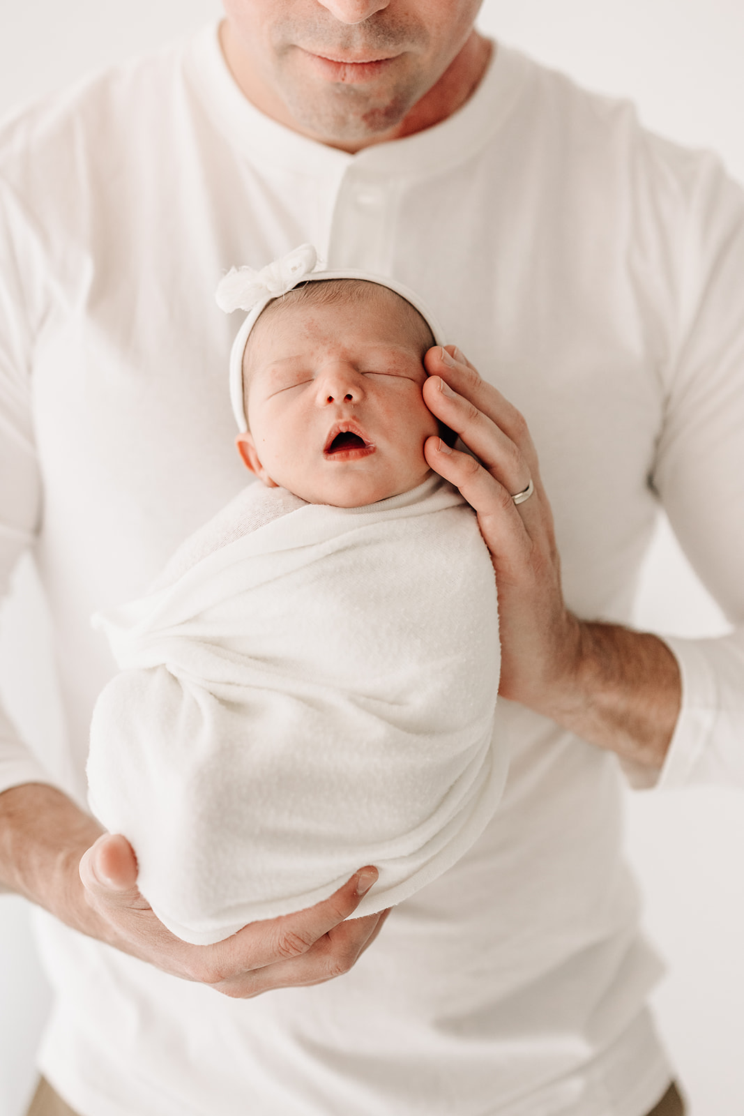 A newborn baby sleeps upright in dad's hands in a studio after meeting Star Of The Sea Doula